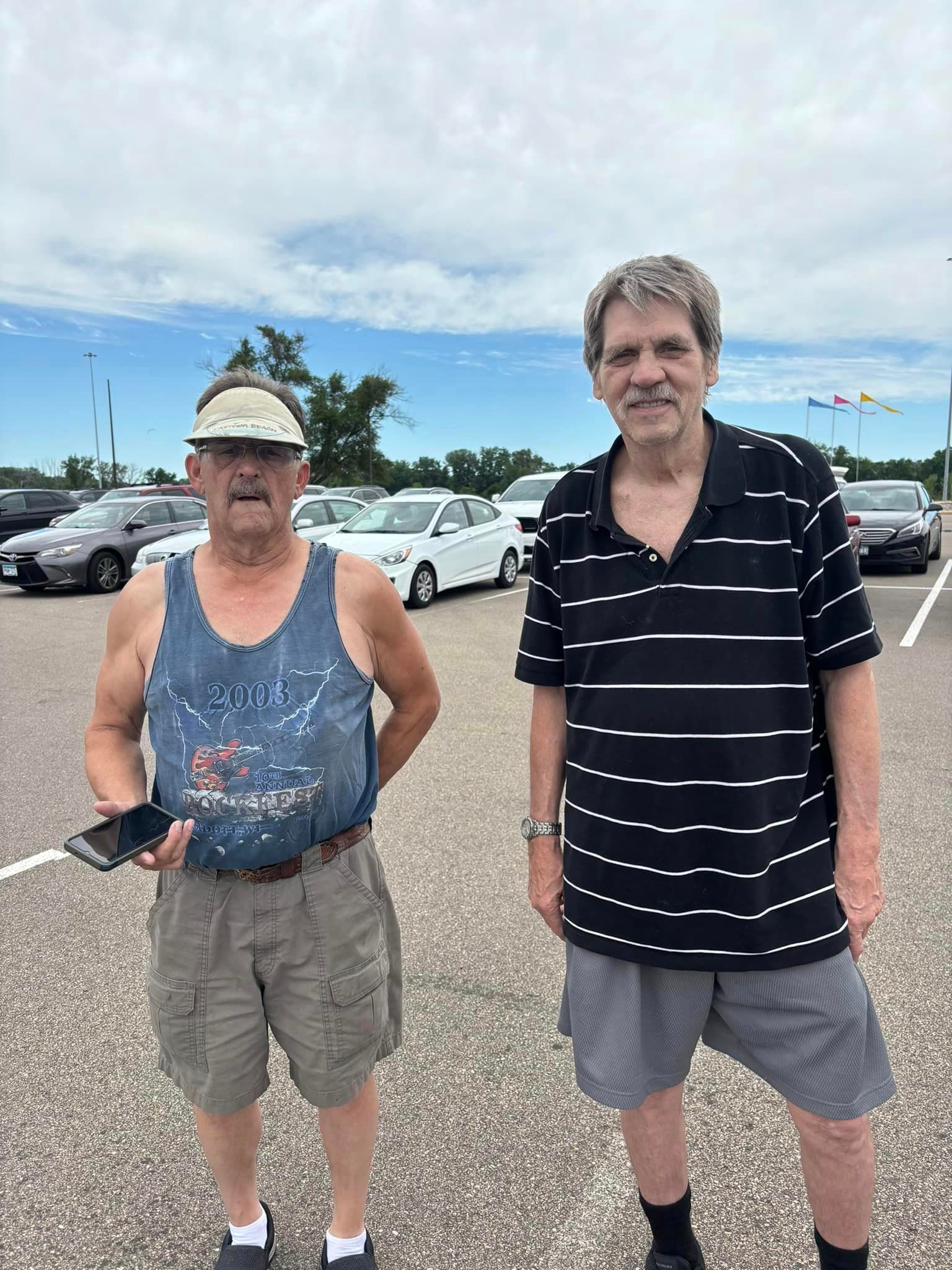 Two men standing in a parking lot on a cloudy day.