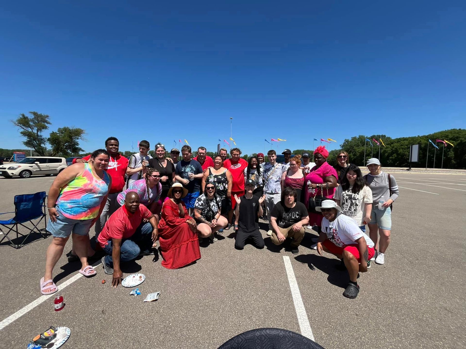 Group of people posing outdoors in parking lot on sunny day.