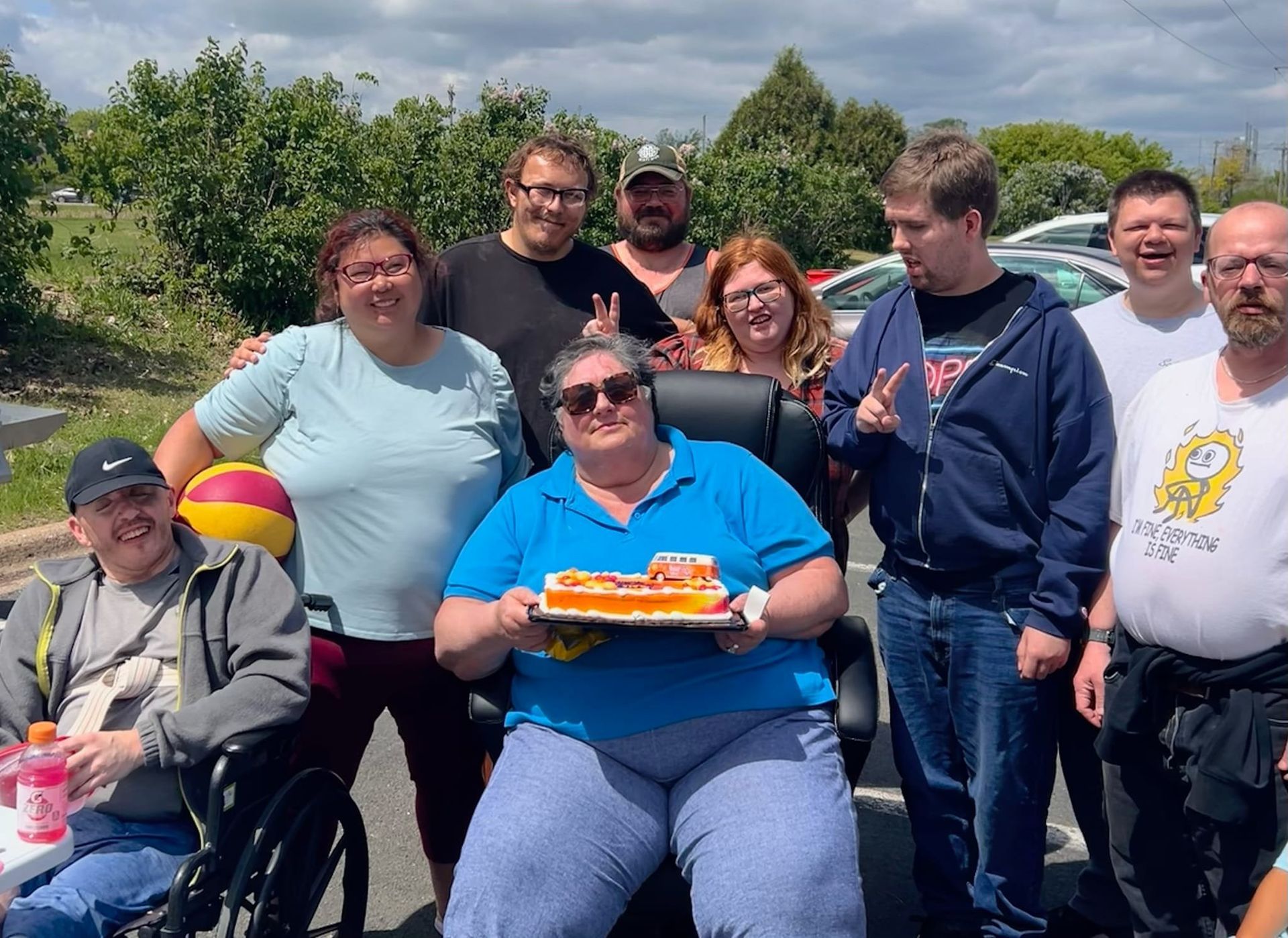 Group of people celebrating with cake outdoors under a cloudy sky.