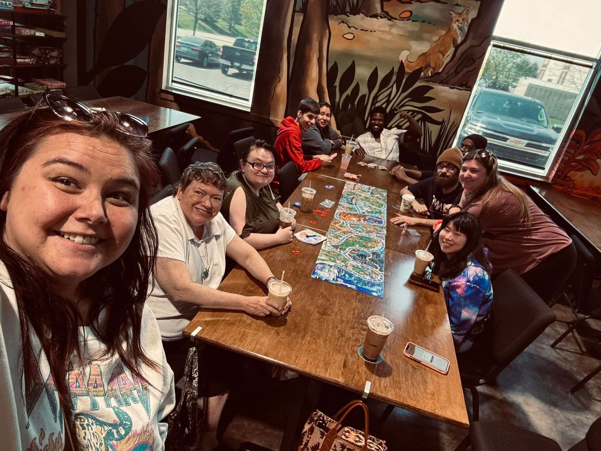 A group of people sitting around a table playing a board game in a cafe. Some people are smiling.
