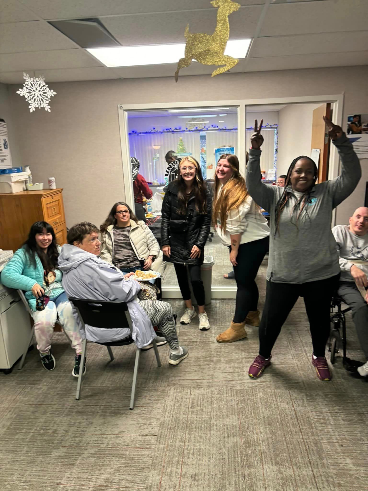 Group of people celebrating in an office decorated for the holidays; one person is making a peace sign.