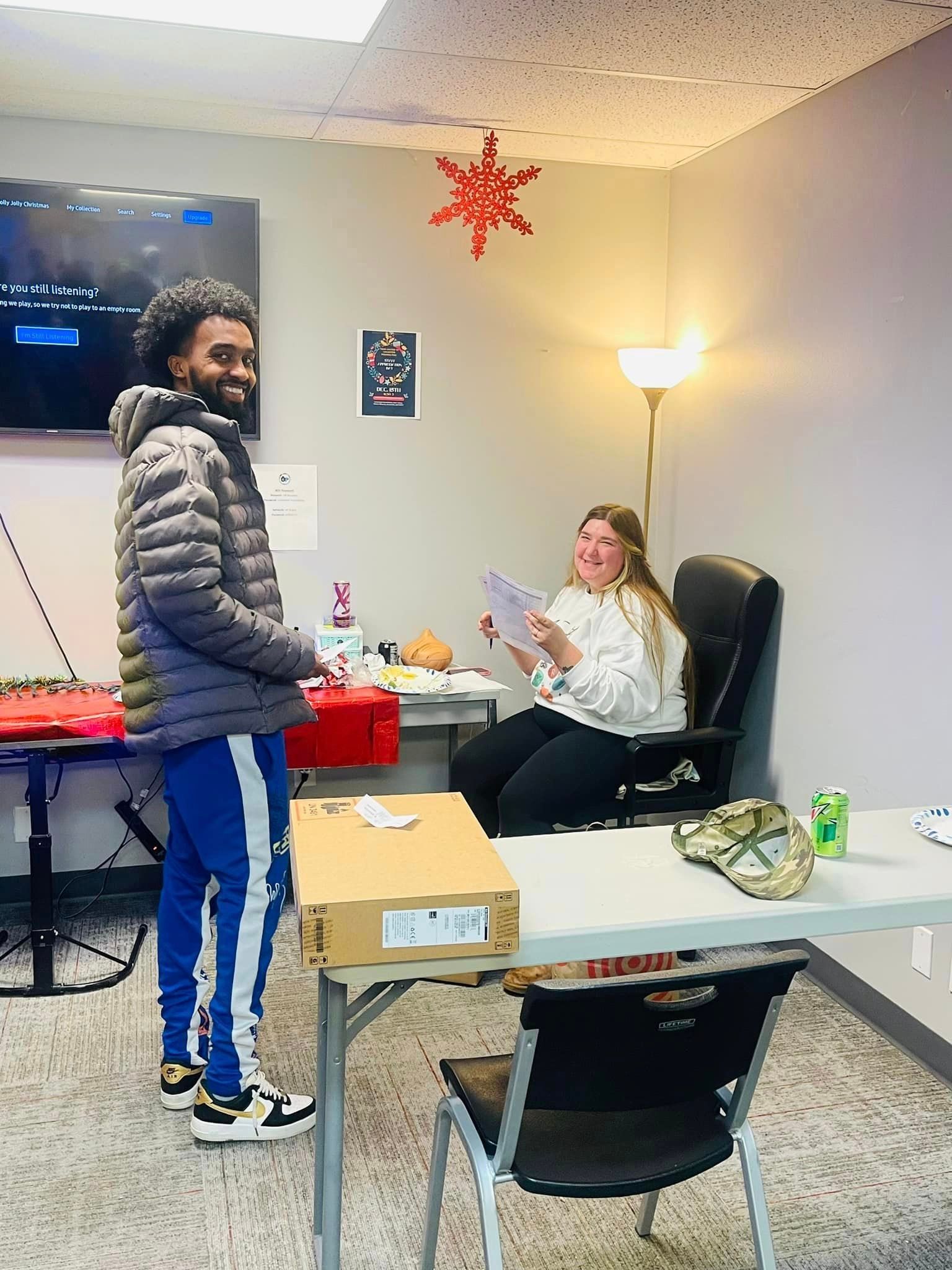 Man with red box and woman with paper in office, decorated for the holidays.