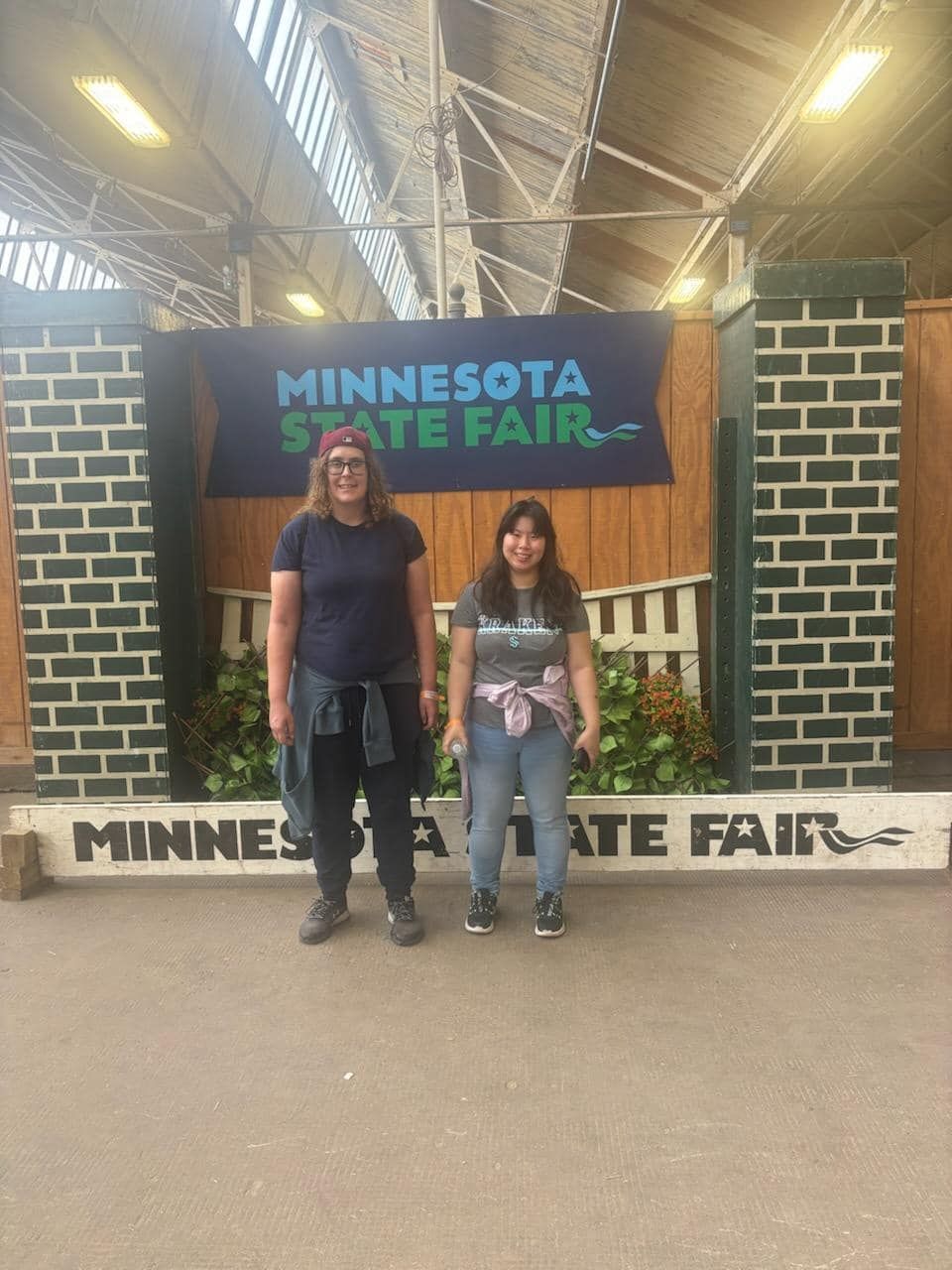 Two people standing in front of a Minnesota State Fair banner.