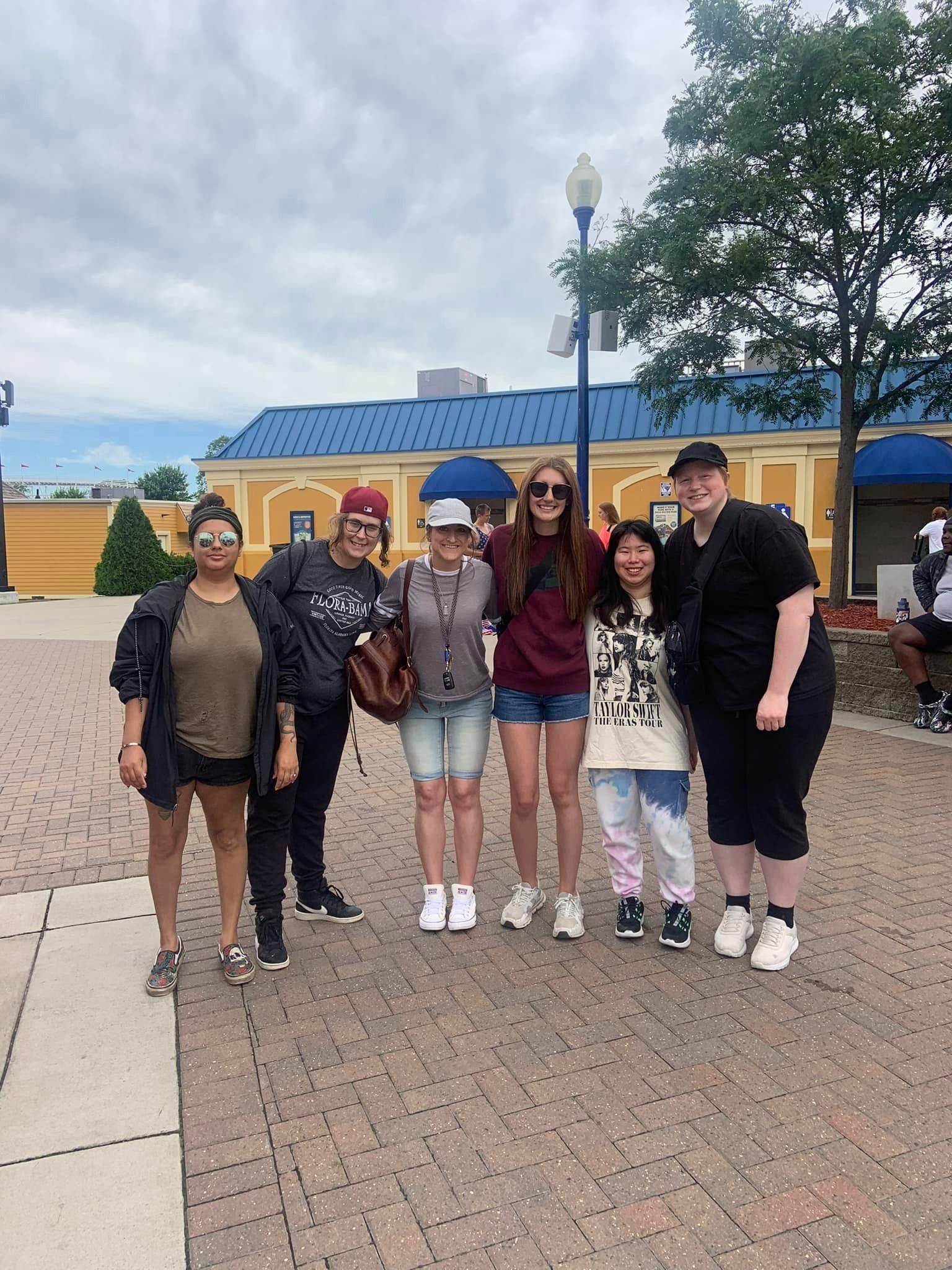 Group of people smiling outside a building, posing for a photo. Cloudy sky overhead.
