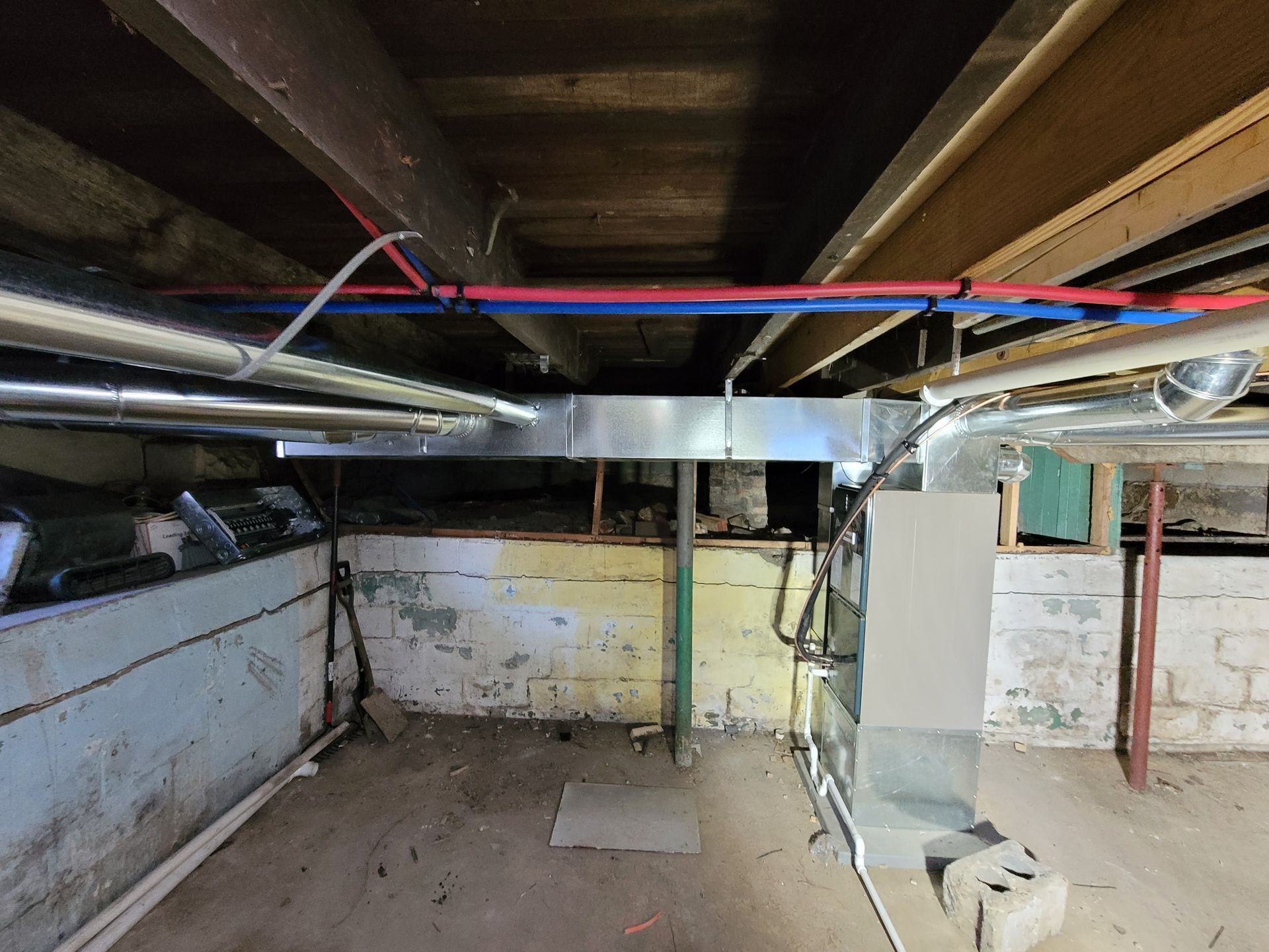 Basement with exposed ceiling beams, ductwork, and plumbing. Concrete walls with peeling paint.