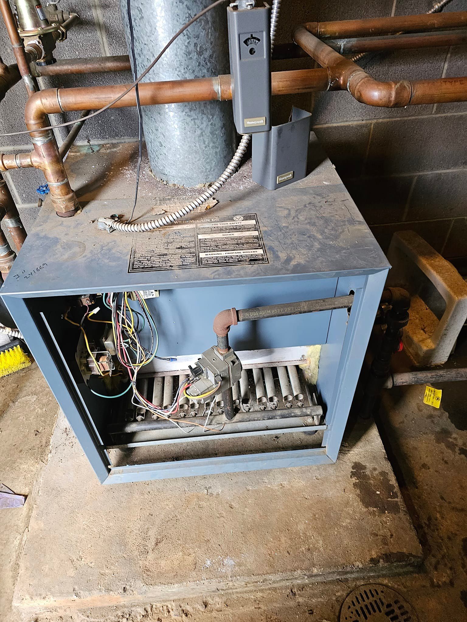 A dirty heater is sitting on top of a concrete floor in a basement.