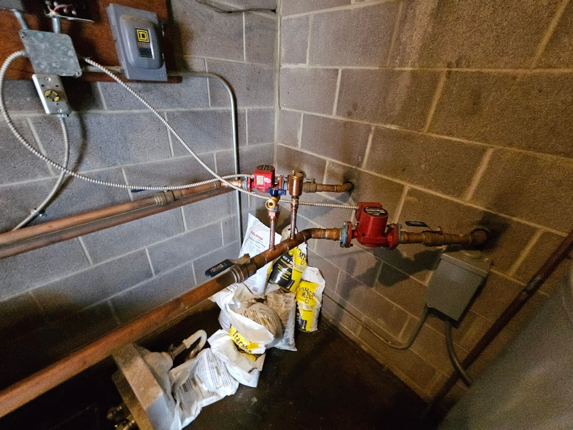 A corner of a room with a brick wall and pipes.