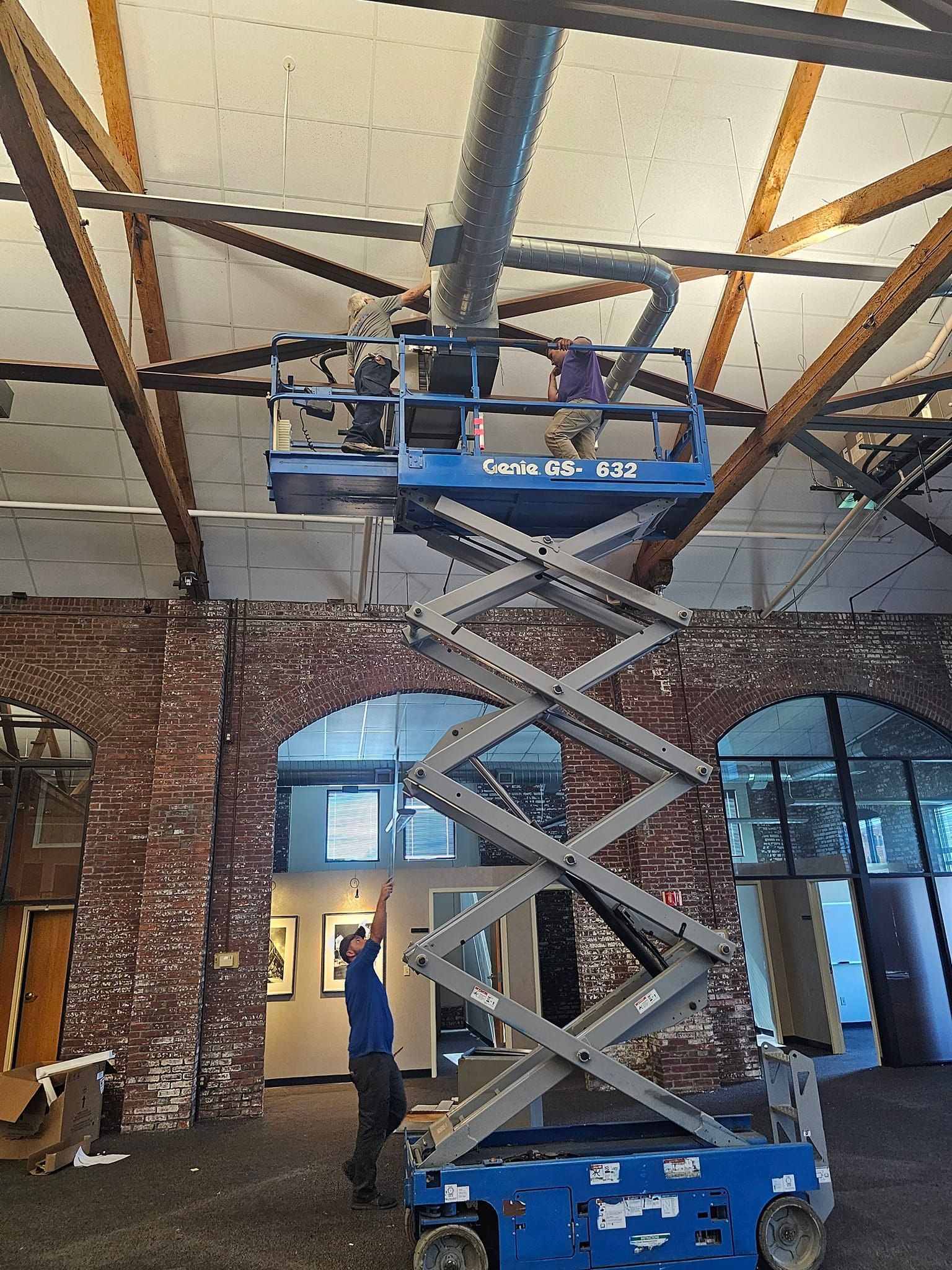 A man is standing on a scissor lift in a room with a brick wall.