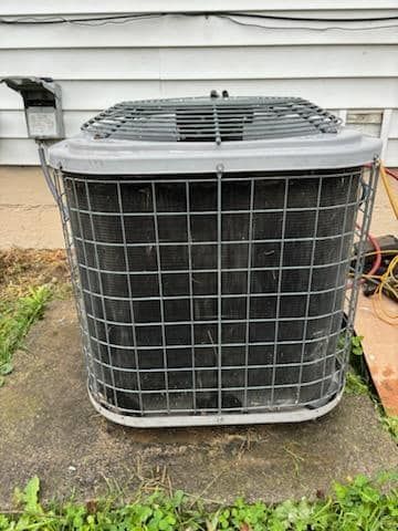A dirty air conditioner is sitting on the ground in front of a house.