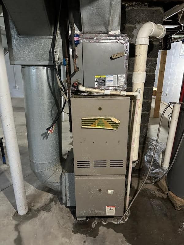 A furnace is sitting in a basement next to a pipe.