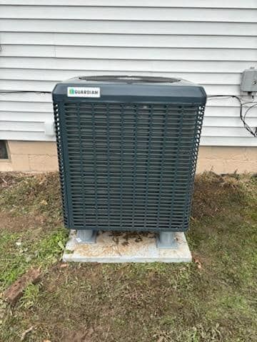 A large air conditioner is sitting in the grass in front of a house.