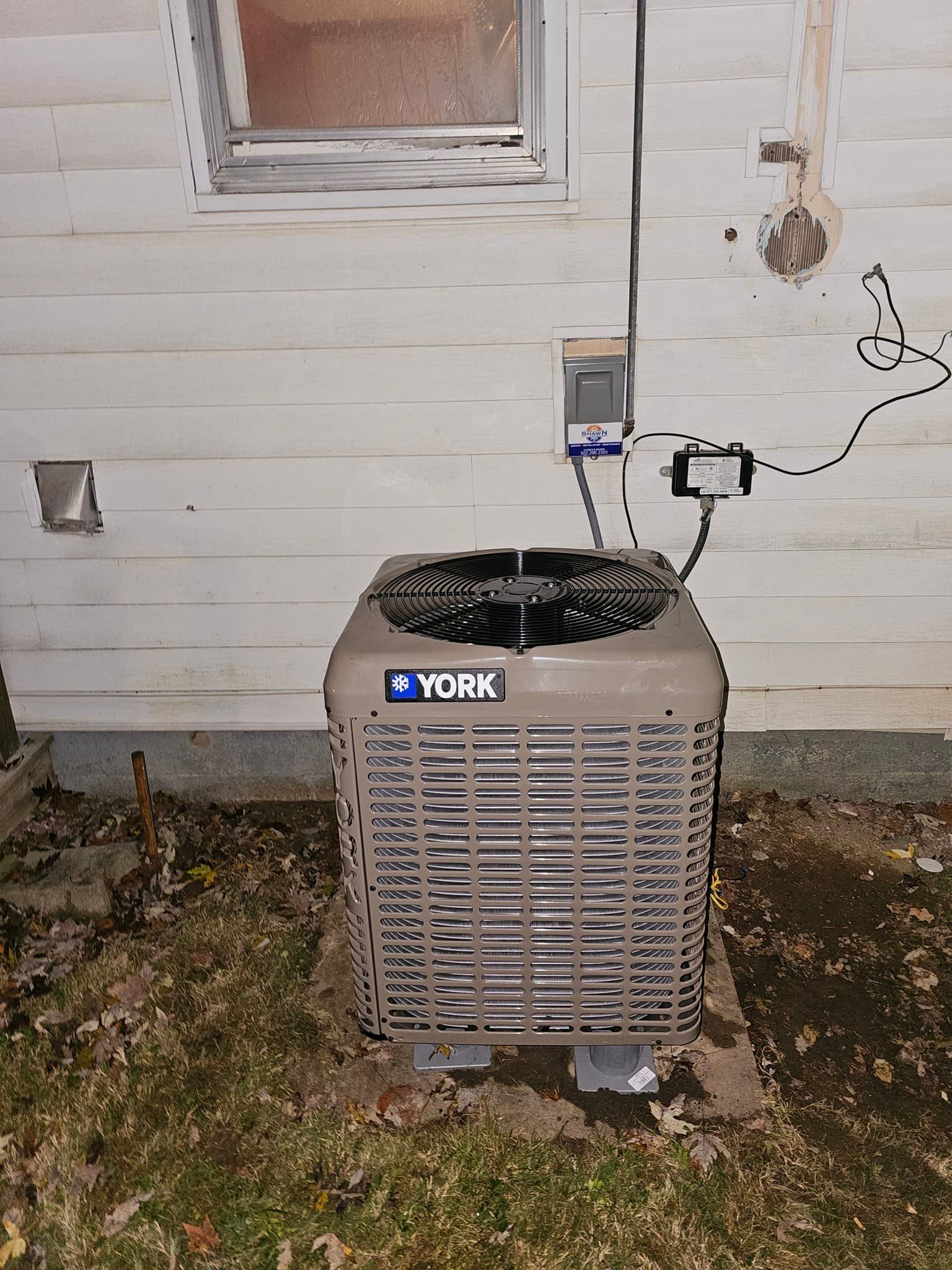 A york air conditioner is sitting outside of a house.