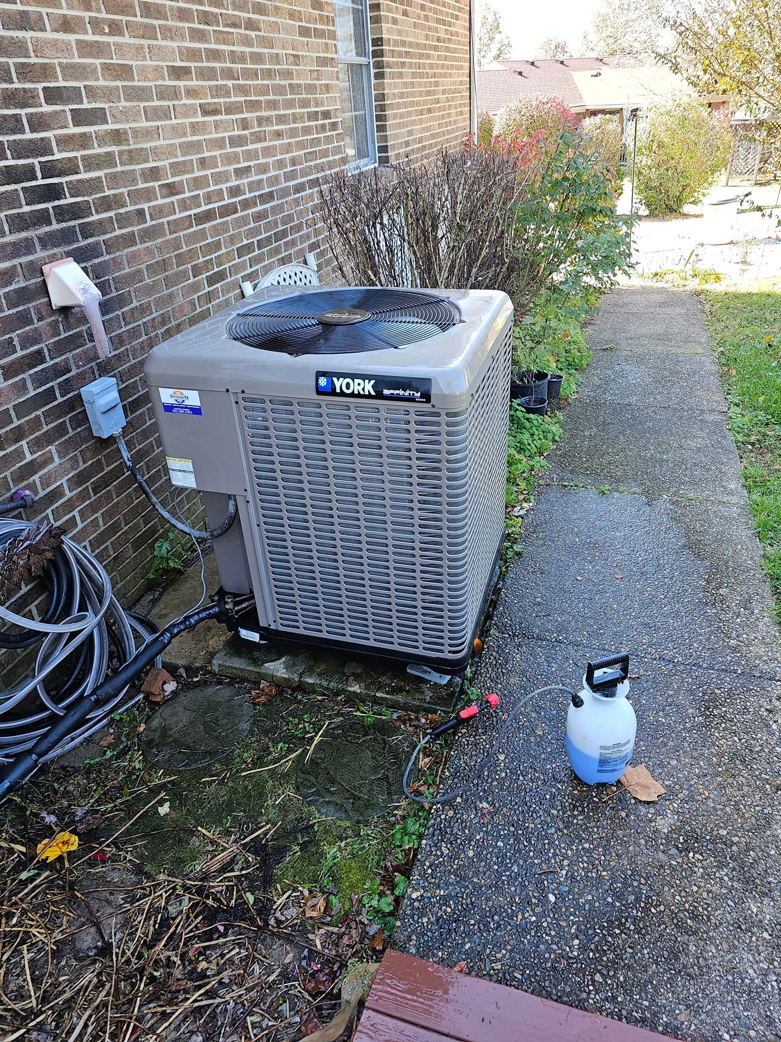 An air conditioner is sitting on the side of a brick building next to a sidewalk.