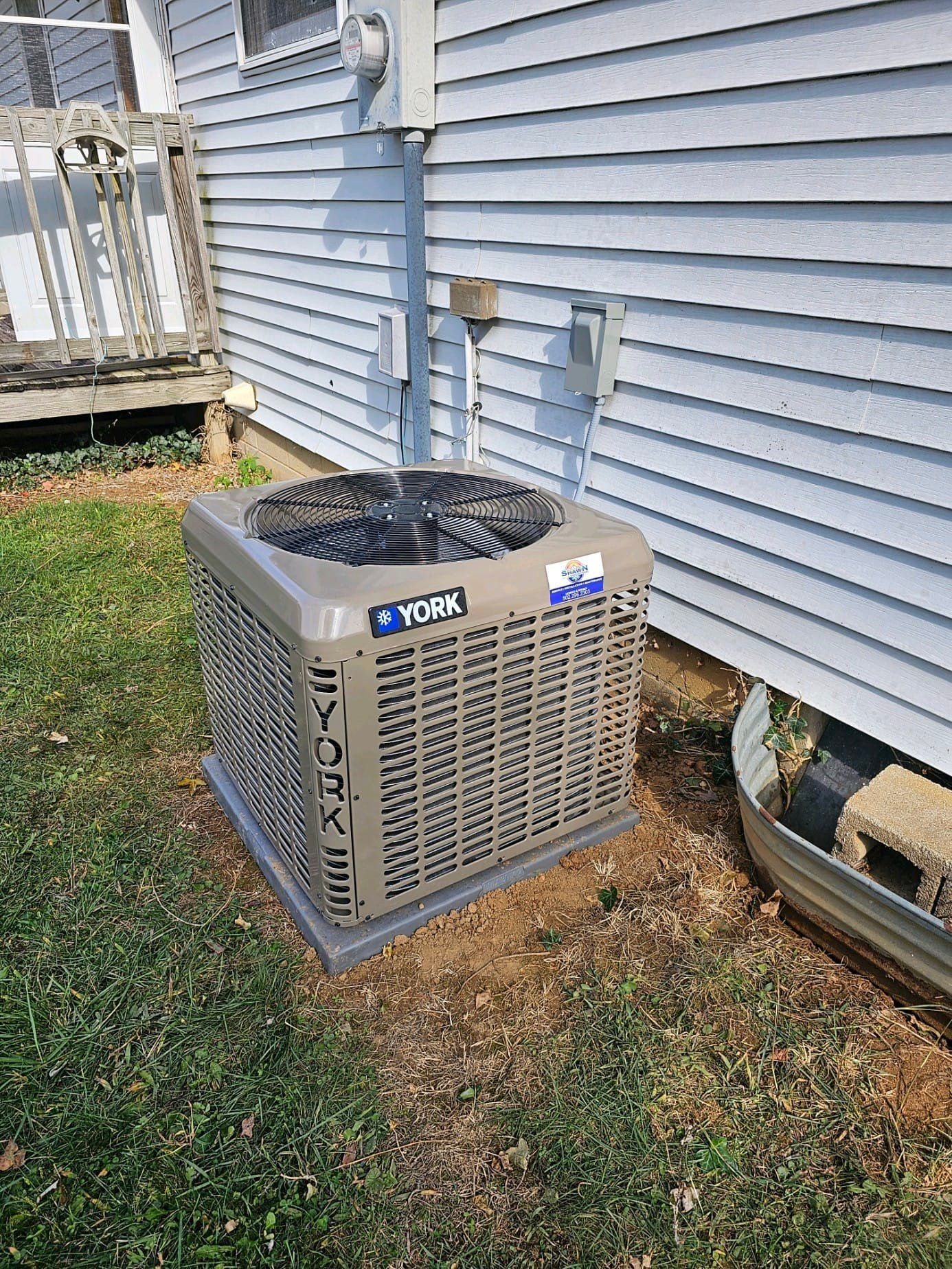 A york air conditioner is sitting on the ground in front of a house.