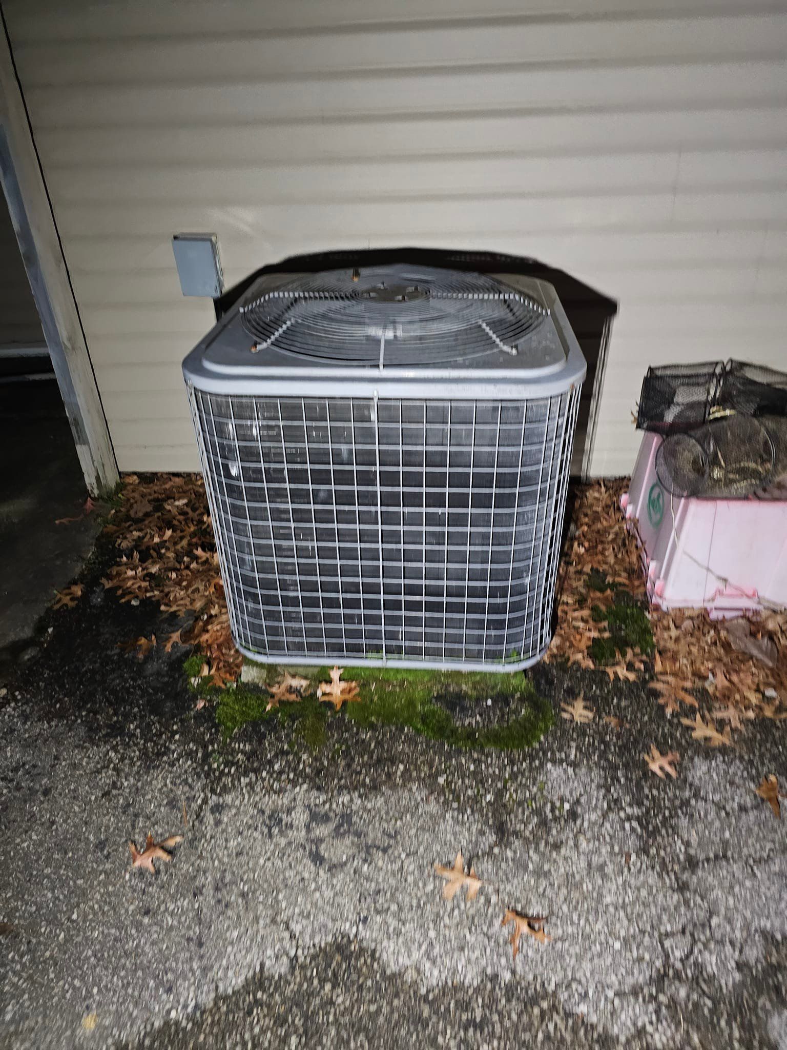 An air conditioner is sitting on the ground outside of a house.