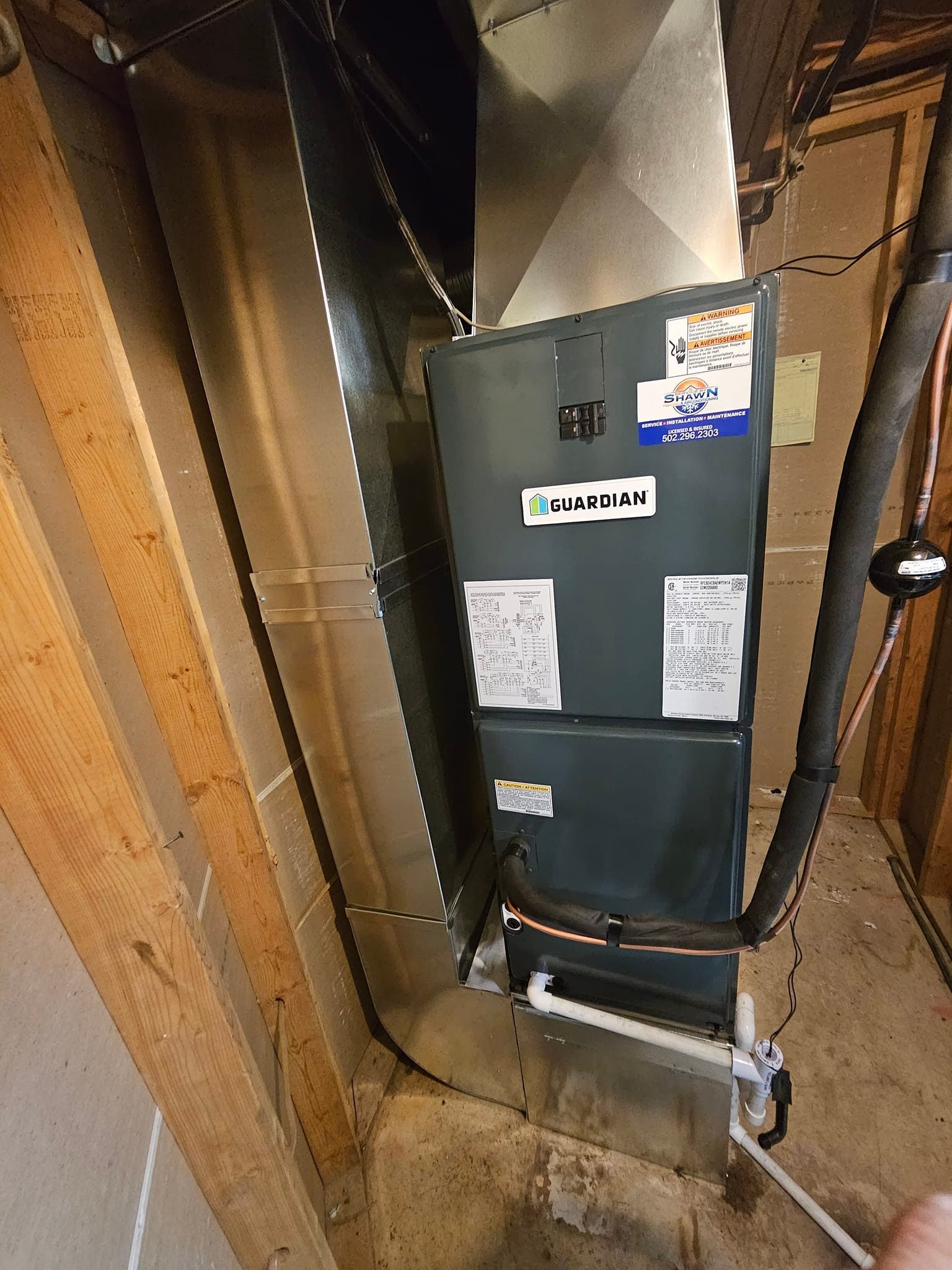 A person is holding a hose next to a furnace in a basement.