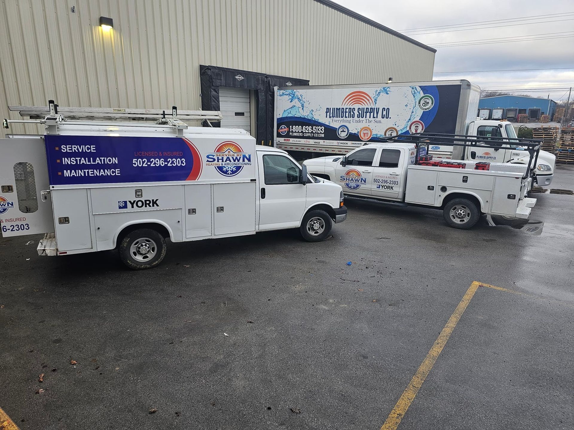 Two utility trucks are parked in a parking lot in front of a building.