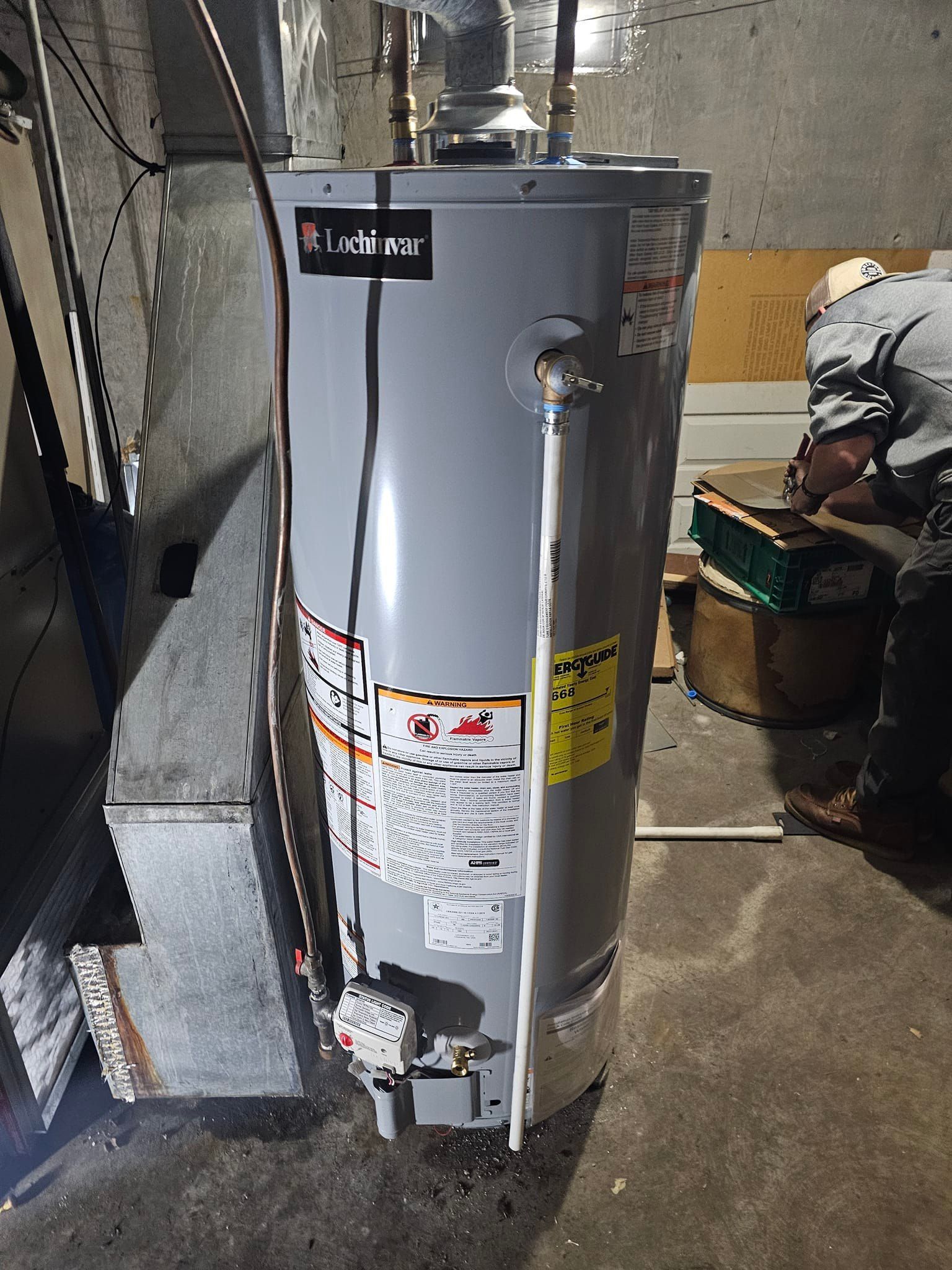 A man is working on a gas water heater in a garage.