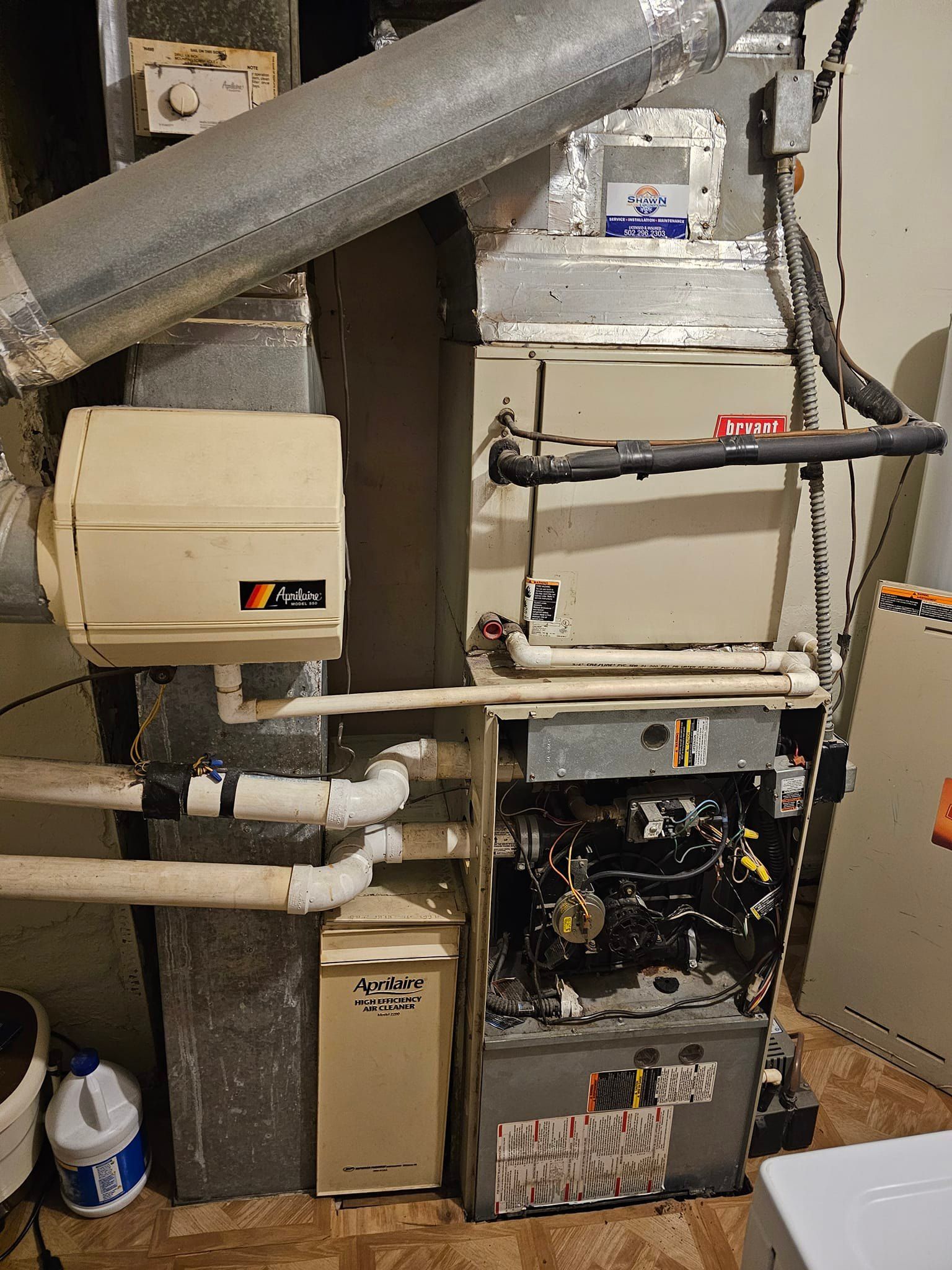 A broken furnace is sitting in a basement next to a pipe.