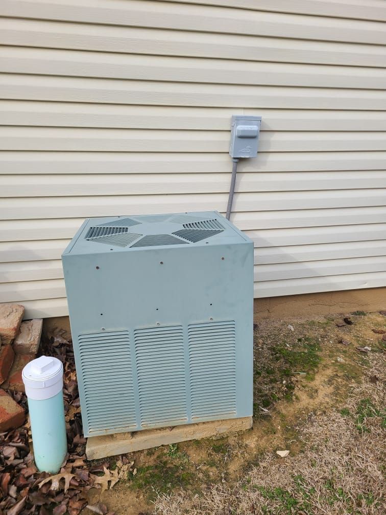 An air conditioner is sitting outside of a house next to a trash can.