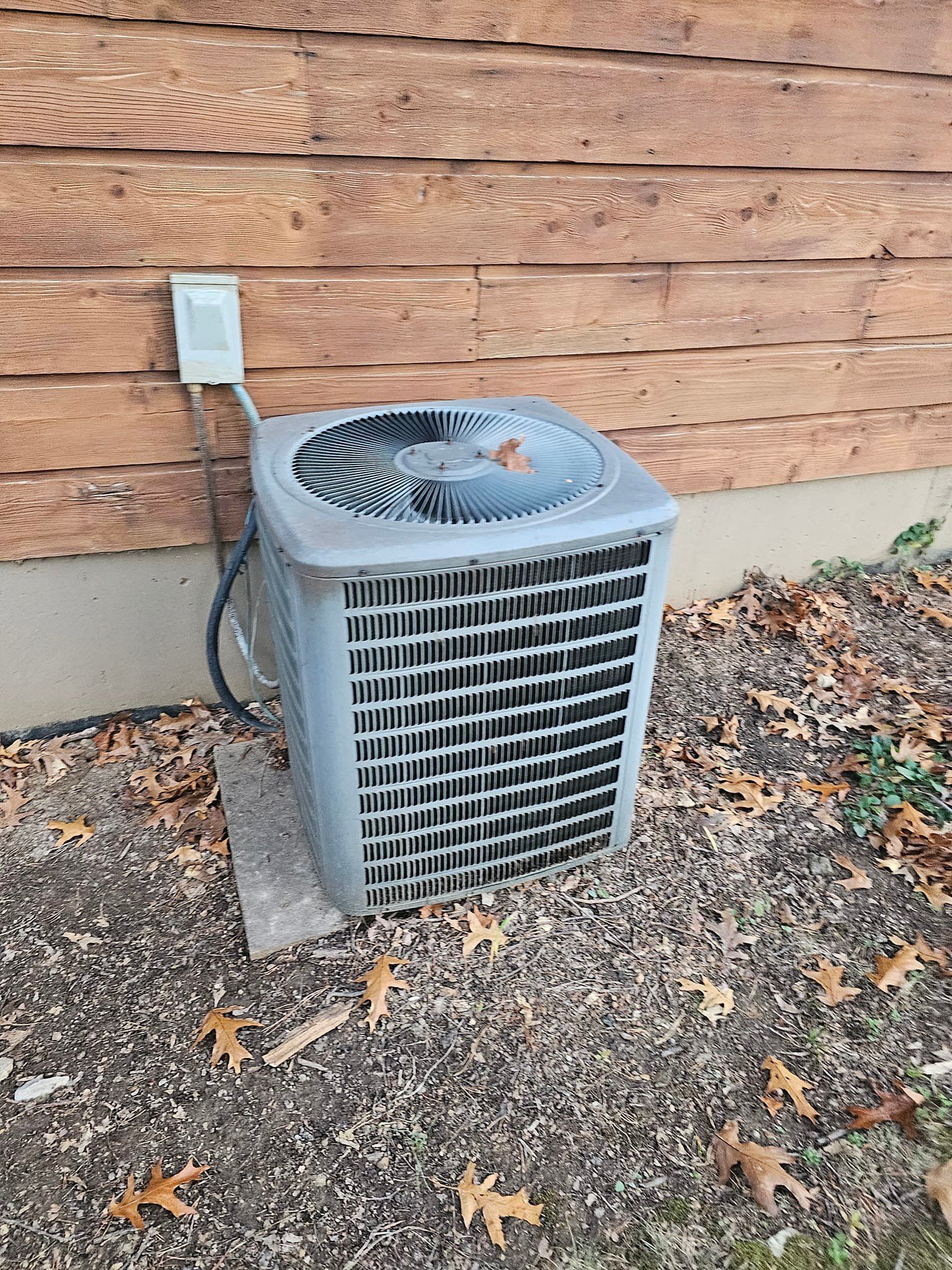 An air conditioner is sitting on the ground next to a wooden wall.