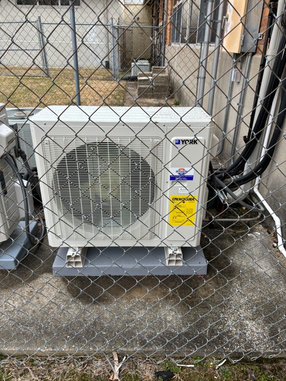 A white air conditioner is sitting next to a chain link fence.