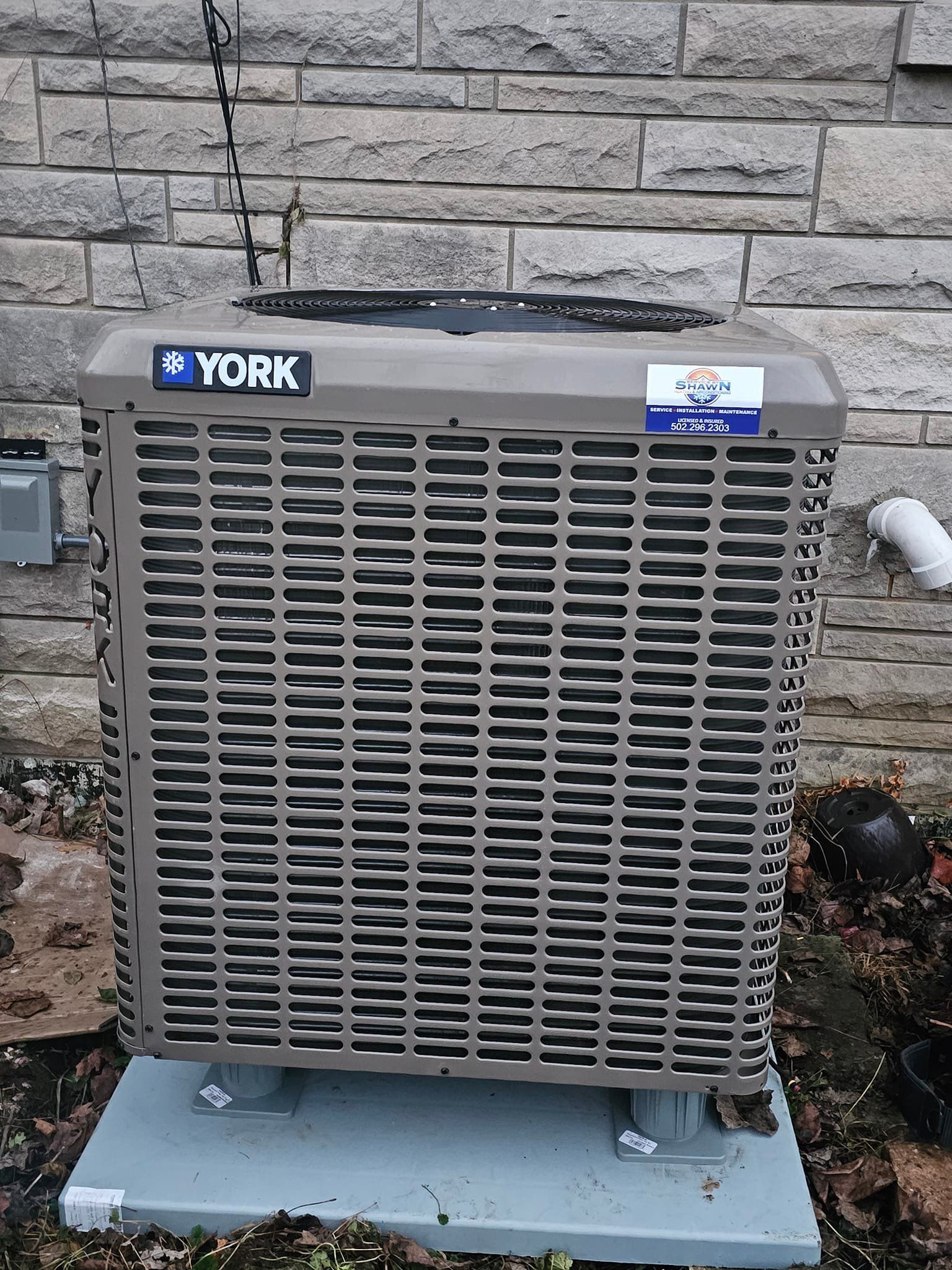 A york air conditioner is sitting in front of a brick wall.