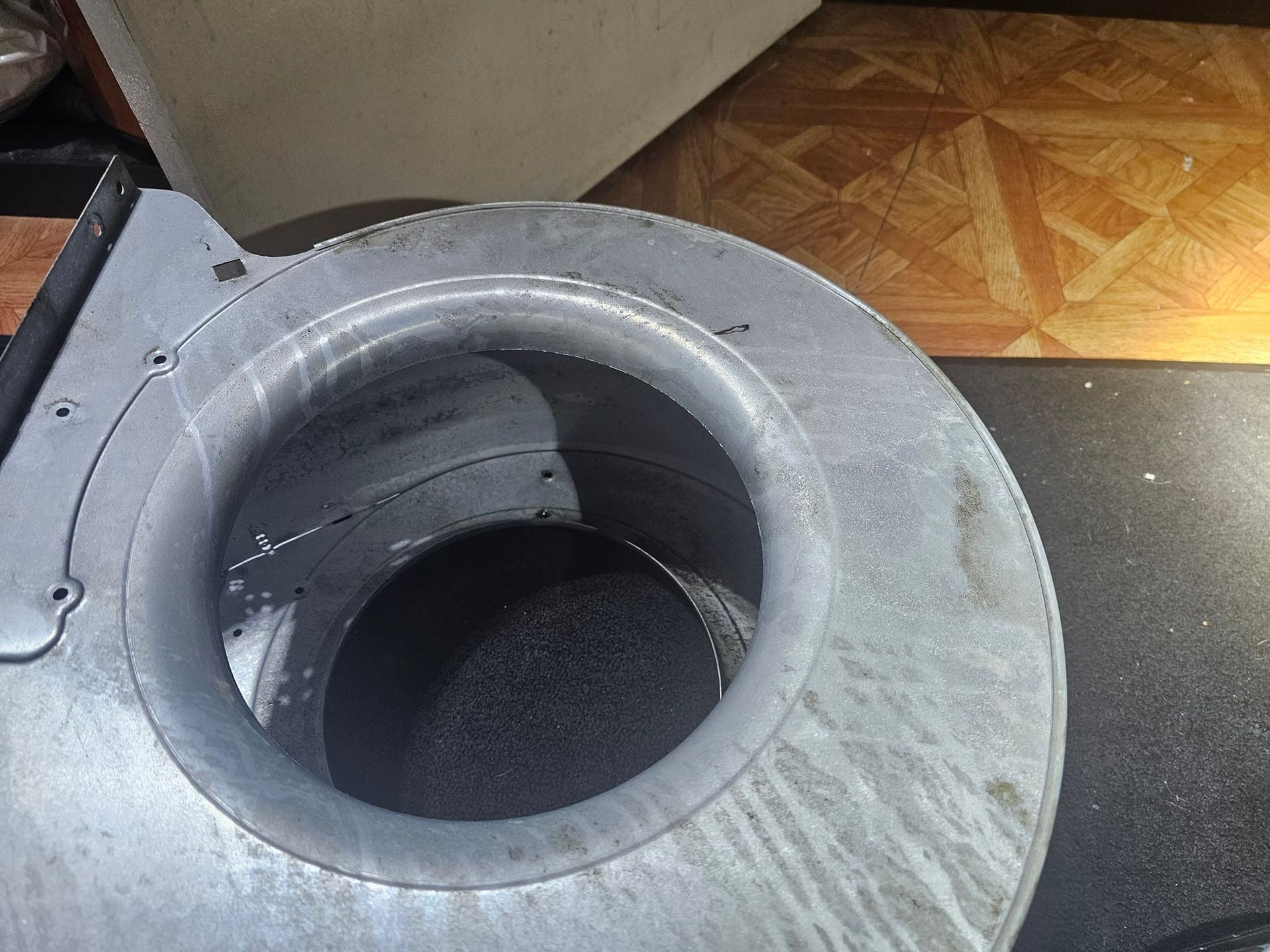 A metal object with a hole in the middle is sitting on a wooden floor.