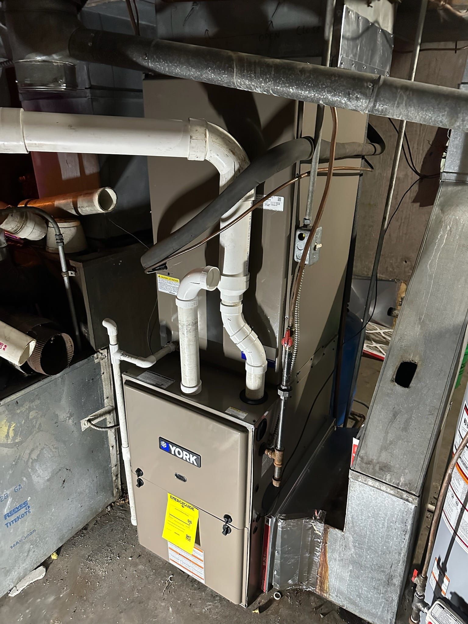 A furnace is sitting in a room with pipes coming out of it.