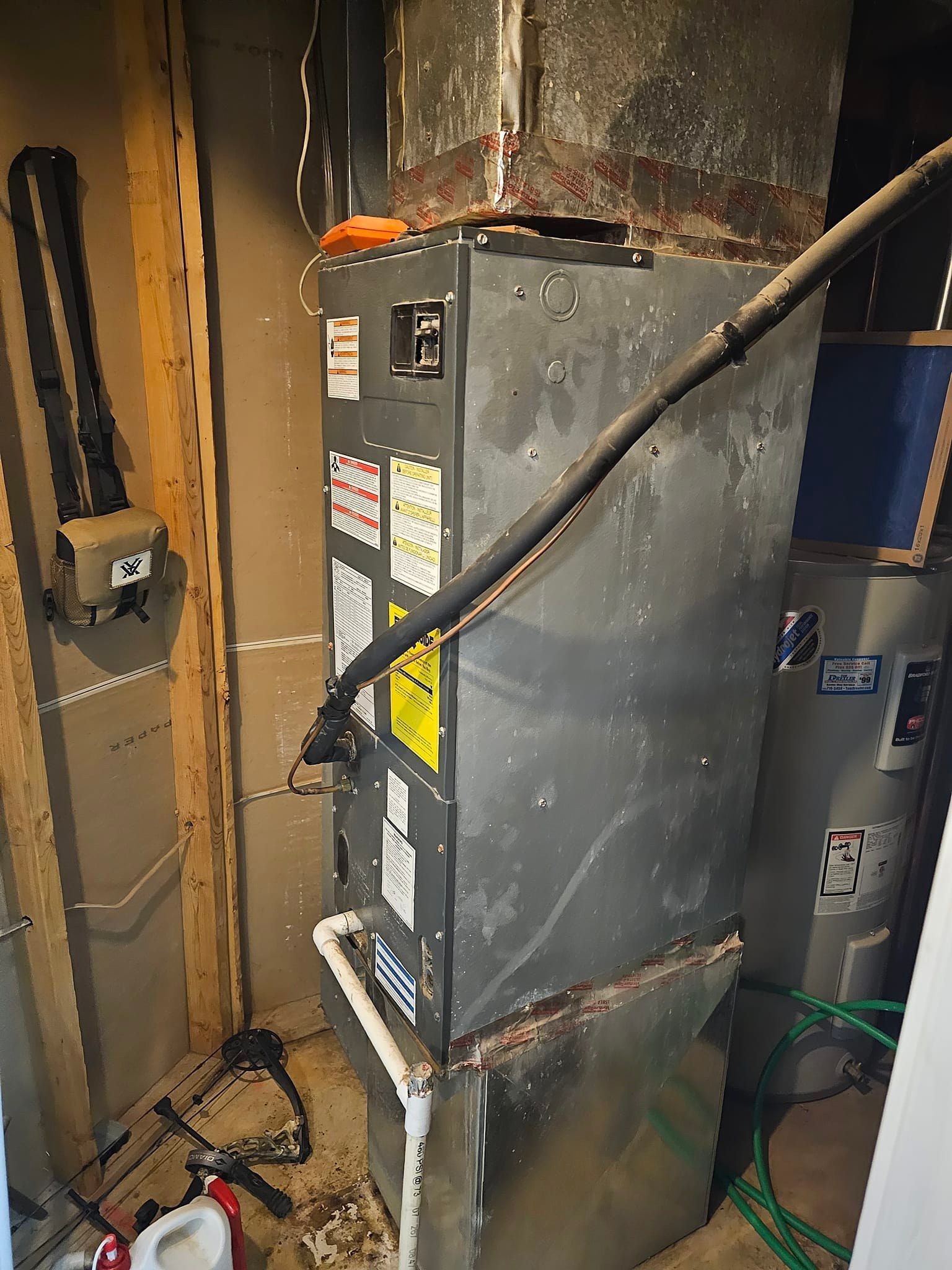 A dirty air conditioner is sitting in a room next to a water heater.