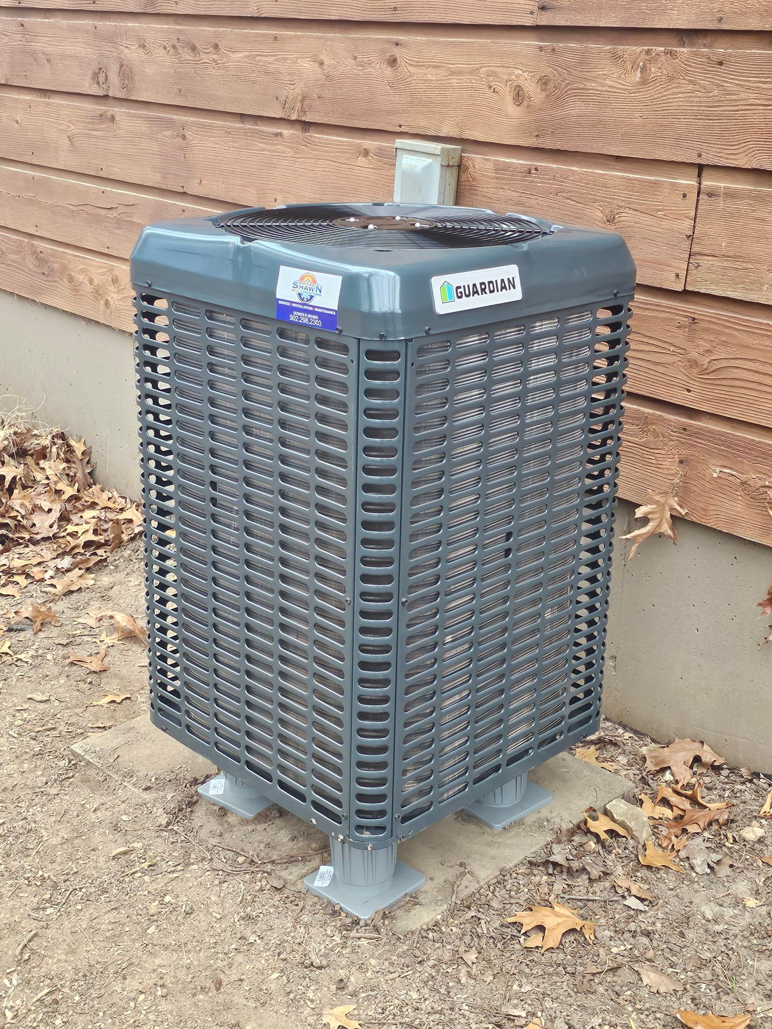 A gray air conditioner is sitting in front of a wooden building.