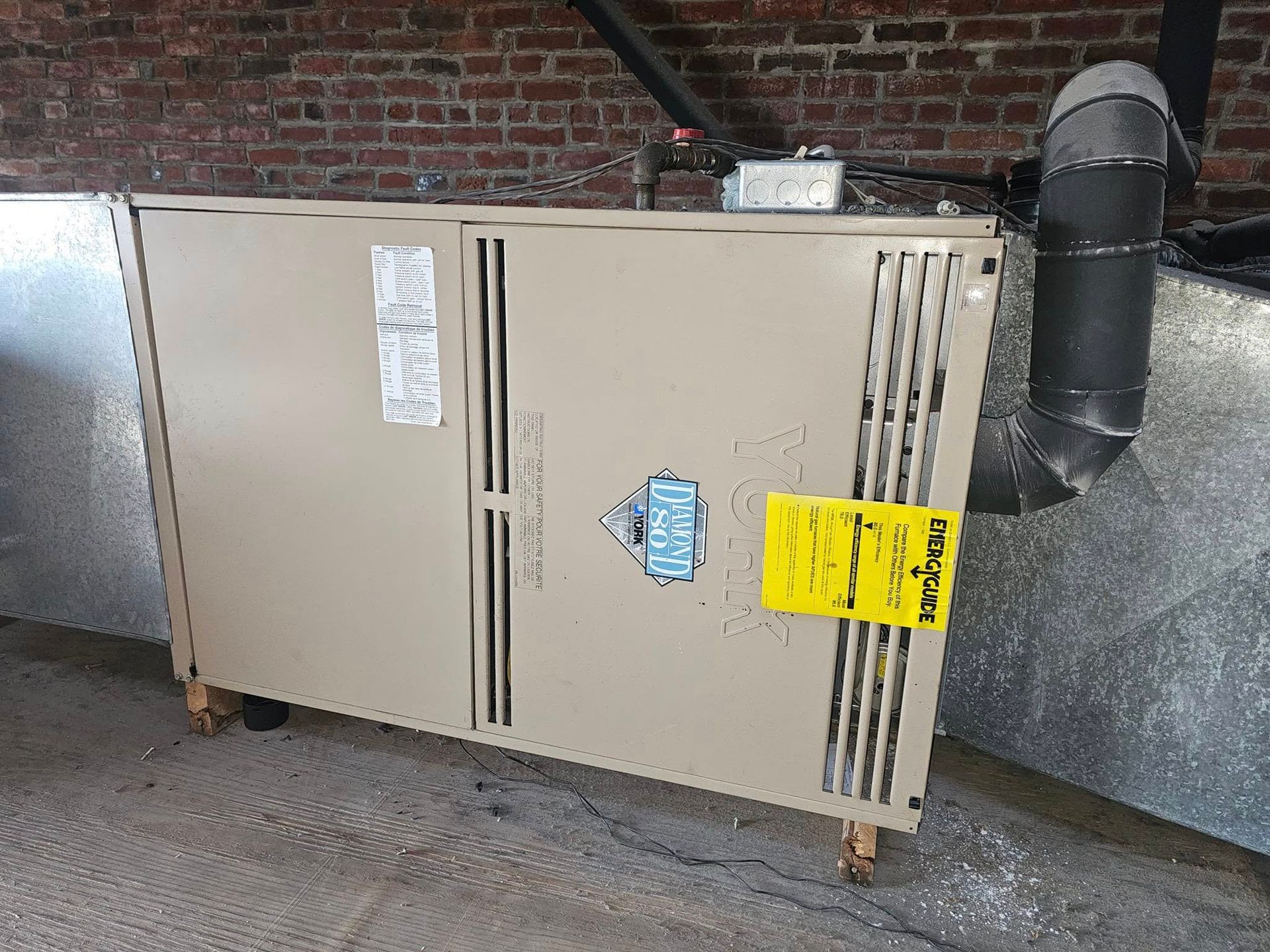 A heater is sitting on the side of a building next to a brick wall.