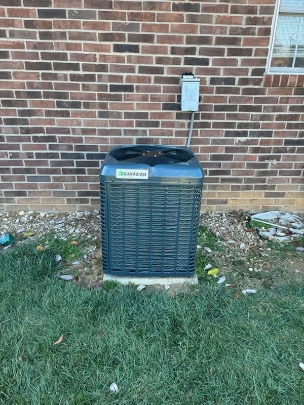 An air conditioner is sitting in the grass in front of a brick building.