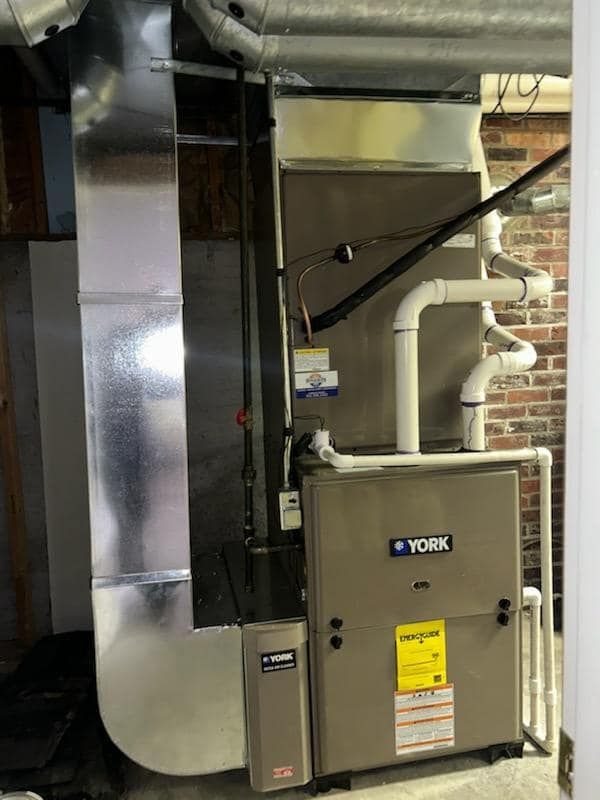 A york air conditioner is sitting in a basement next to a brick wall.