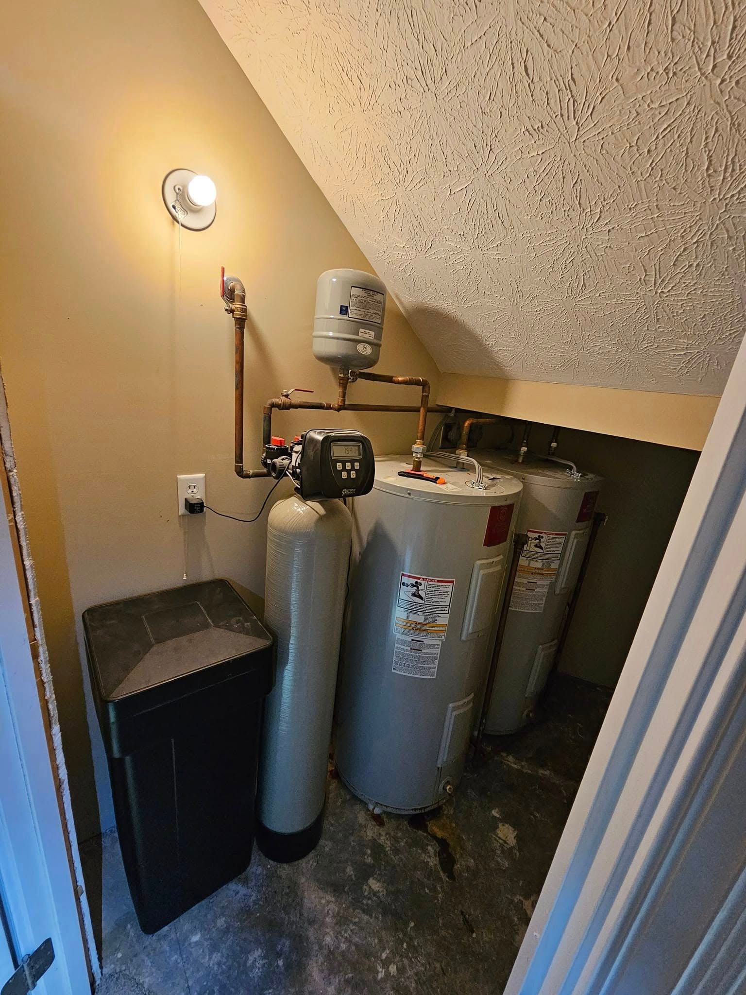 A room with three water heaters and a trash can.