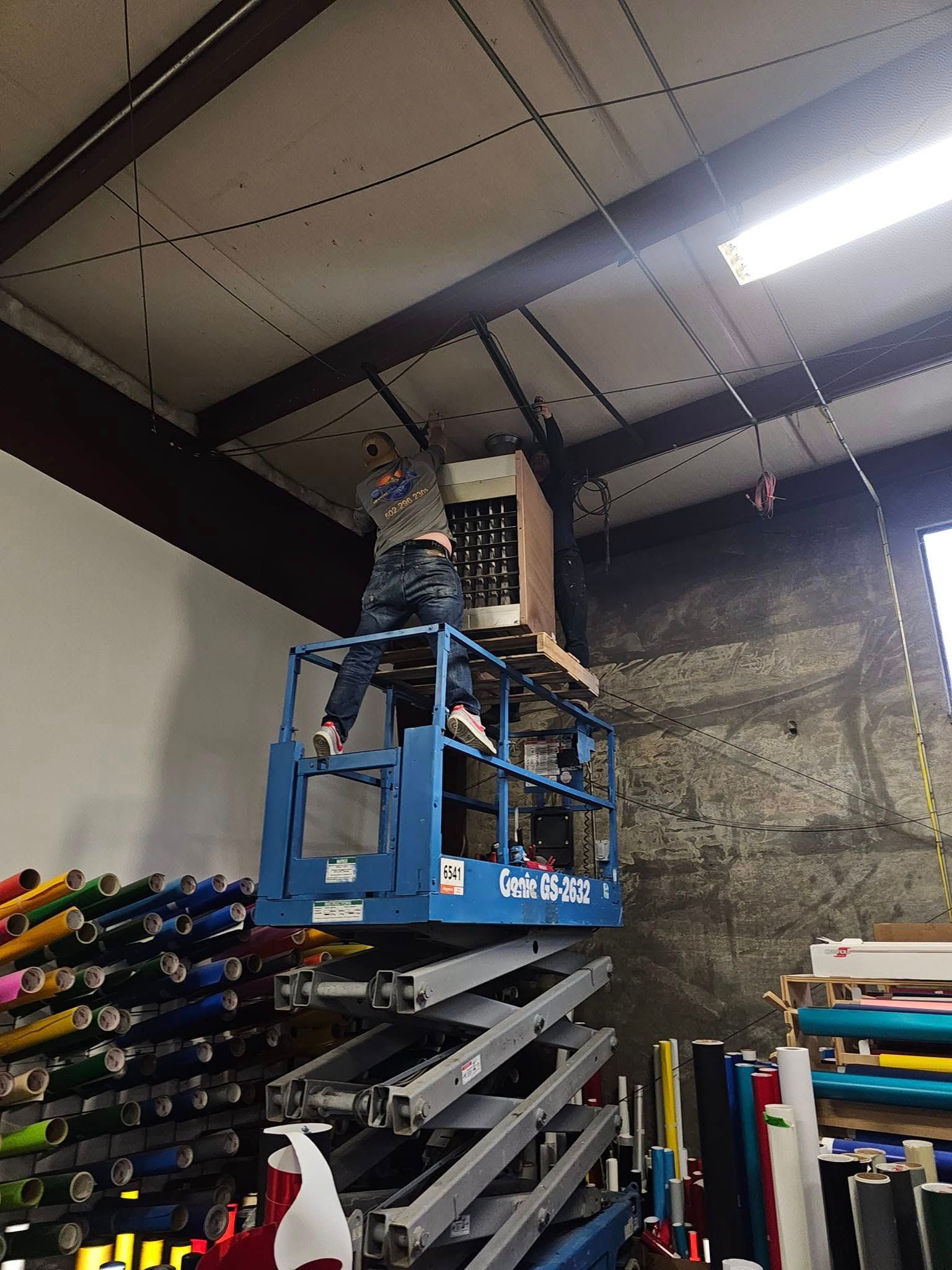 A man is standing on a scissor lift in a warehouse.
