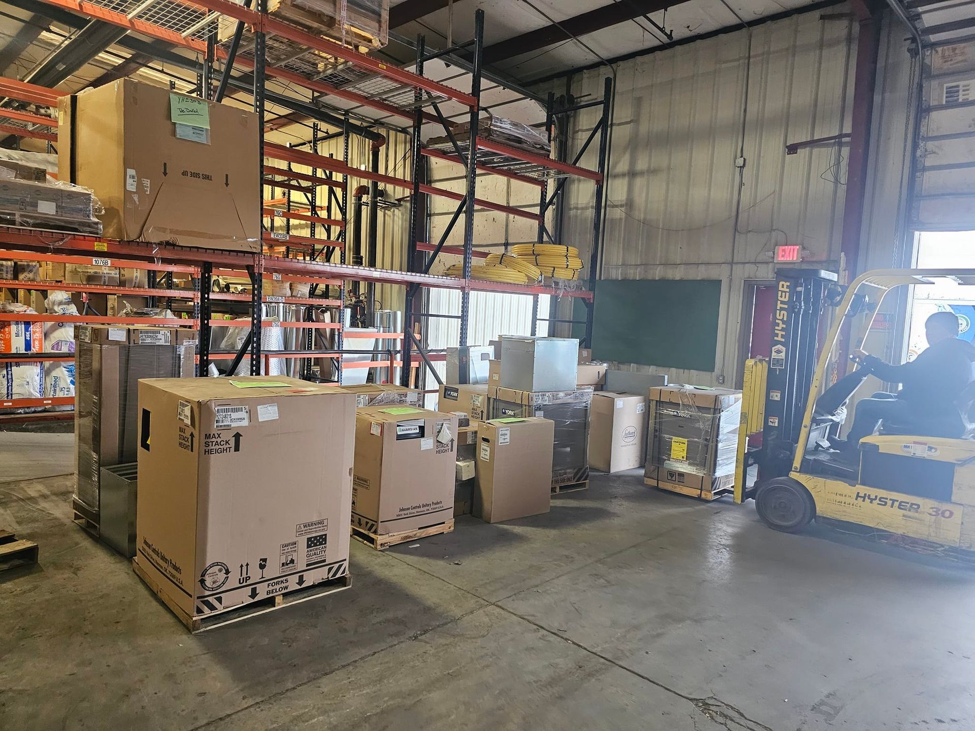 A man is driving a forklift in a warehouse filled with boxes.
