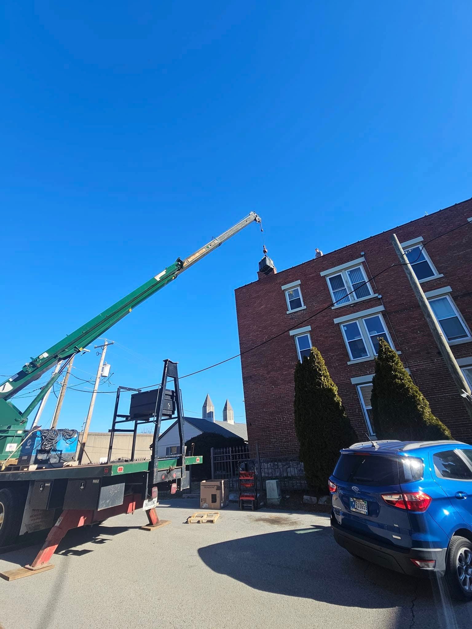 A blue car is parked in front of a brick building with a crane in the background