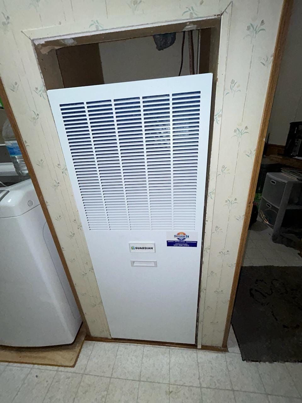 A white air conditioner is sitting in a corner of a room next to a washer and dryer.