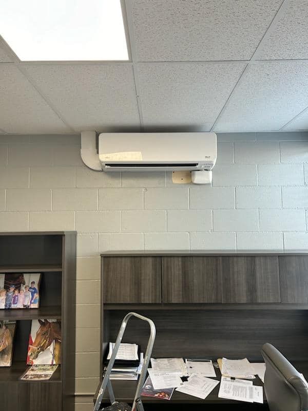 A white air conditioner is mounted on the wall above a desk.