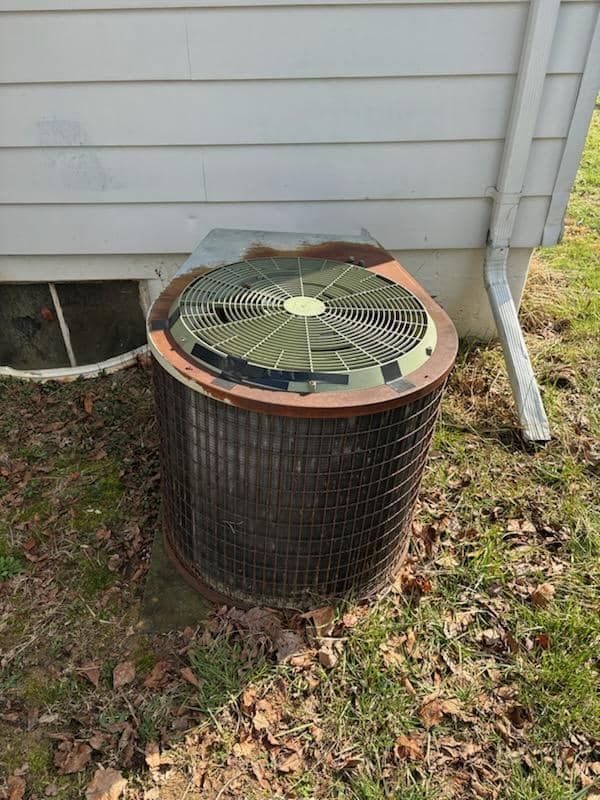 An air conditioner is sitting in the grass next to a house.
