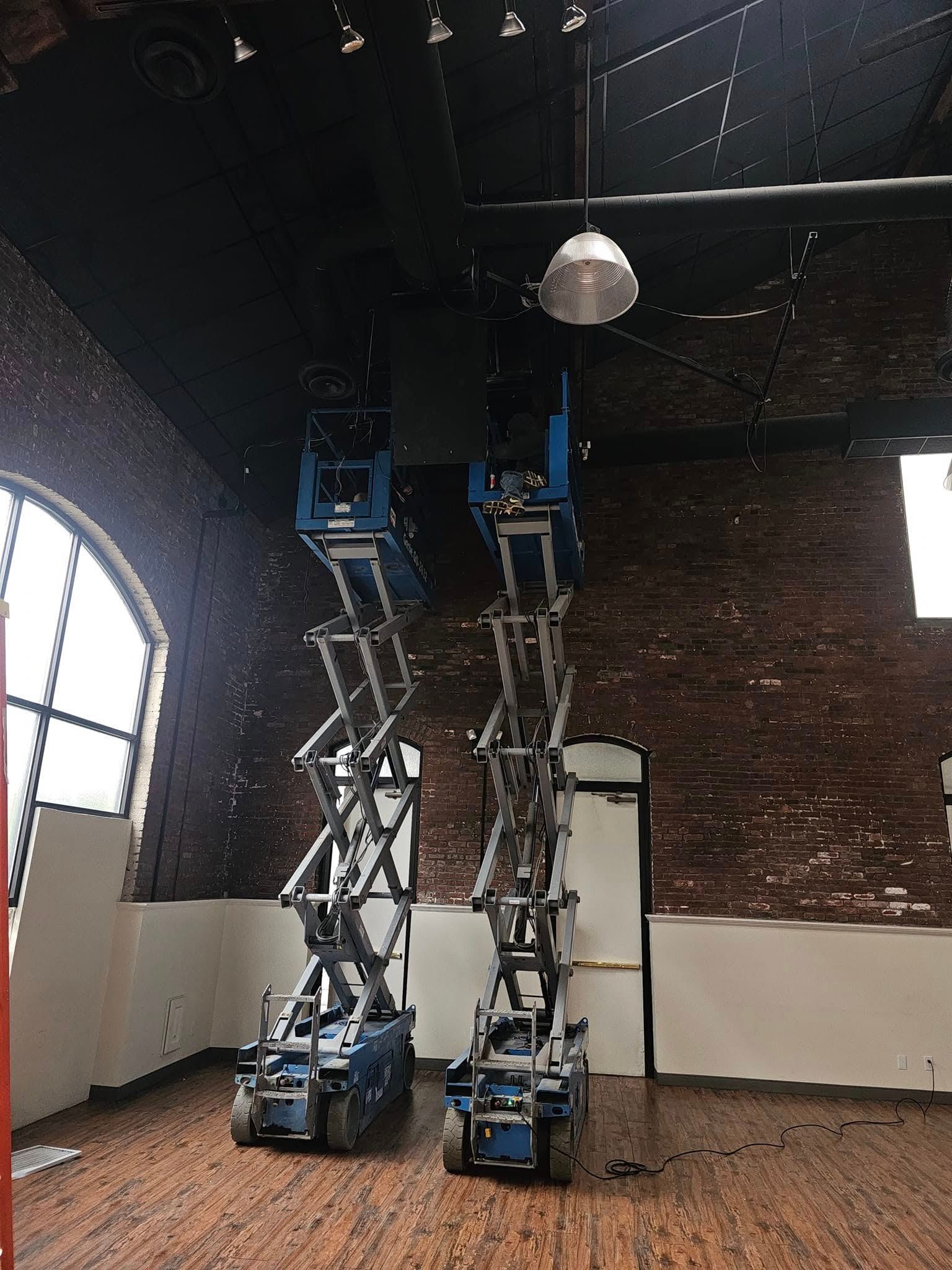 Two scissor lifts in an empty room with a brick wall