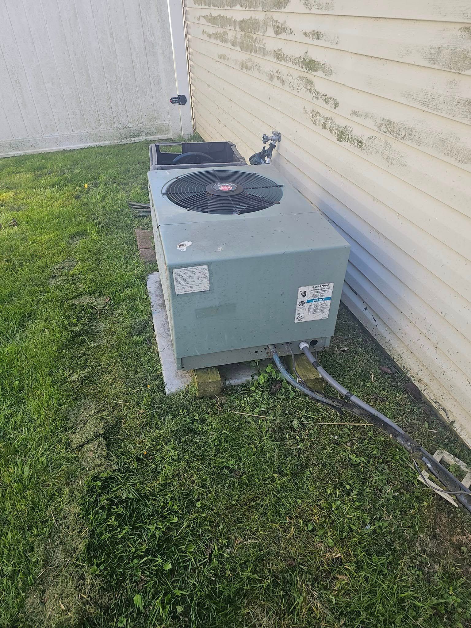 An air conditioner is sitting in the grass next to a building.