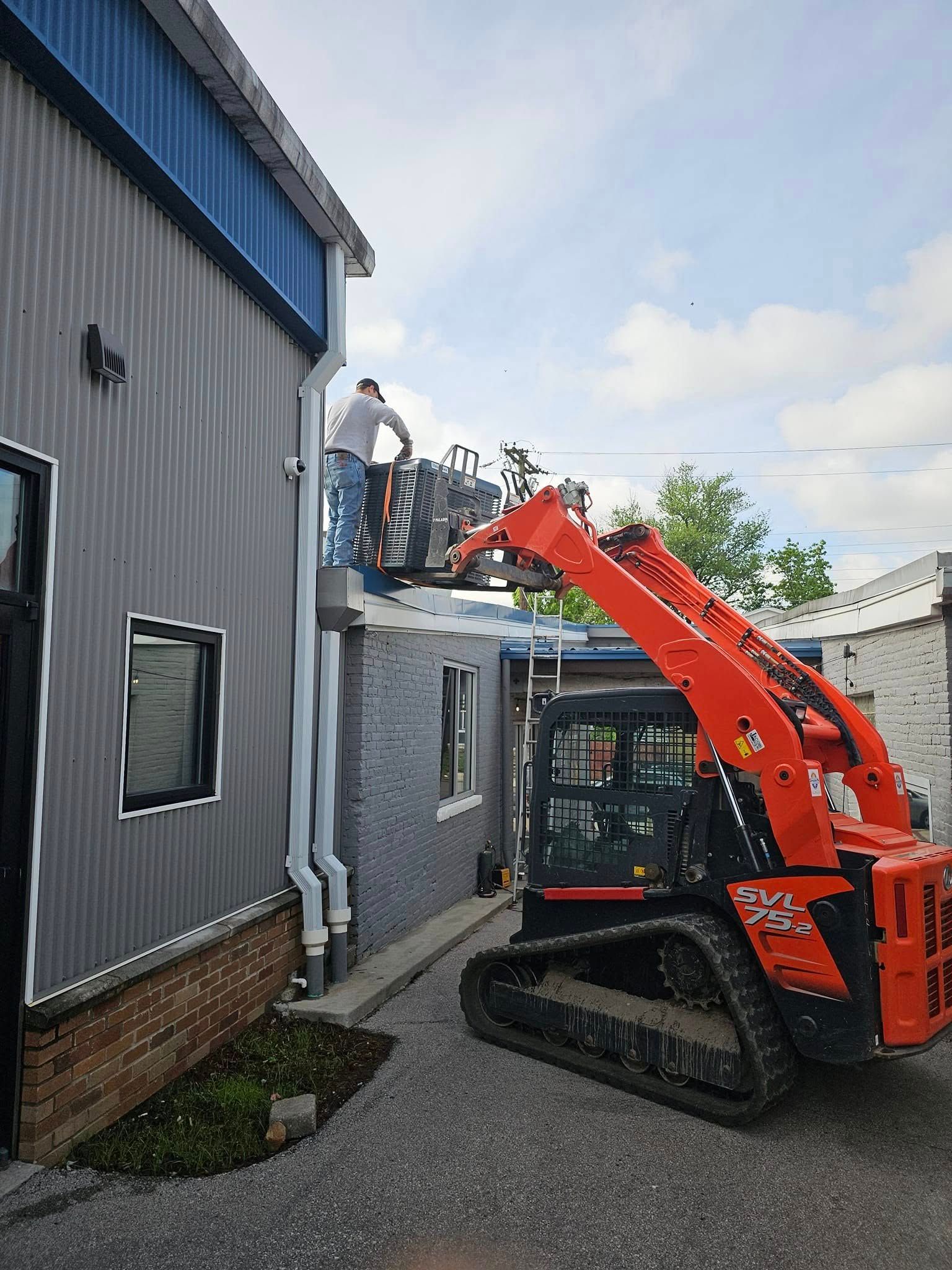 A man is standing on top of a building next to a bulldozer.