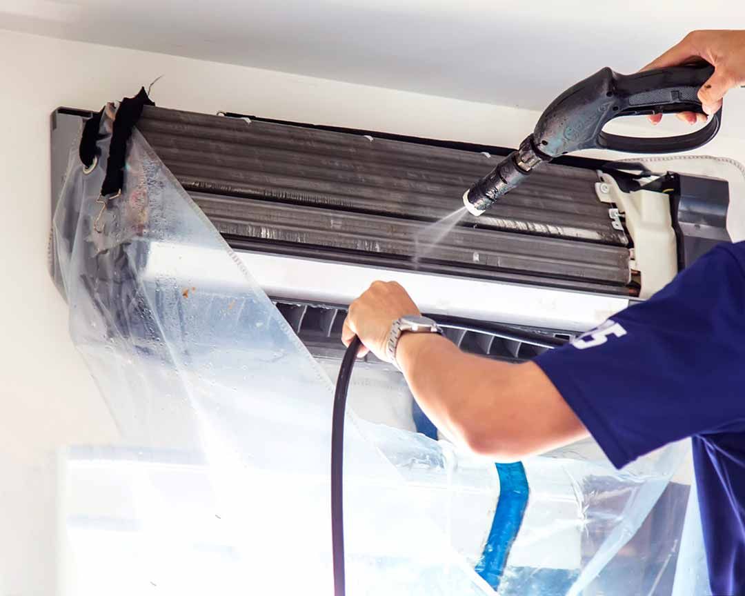 A man is cleaning an air conditioner with a high pressure washer.