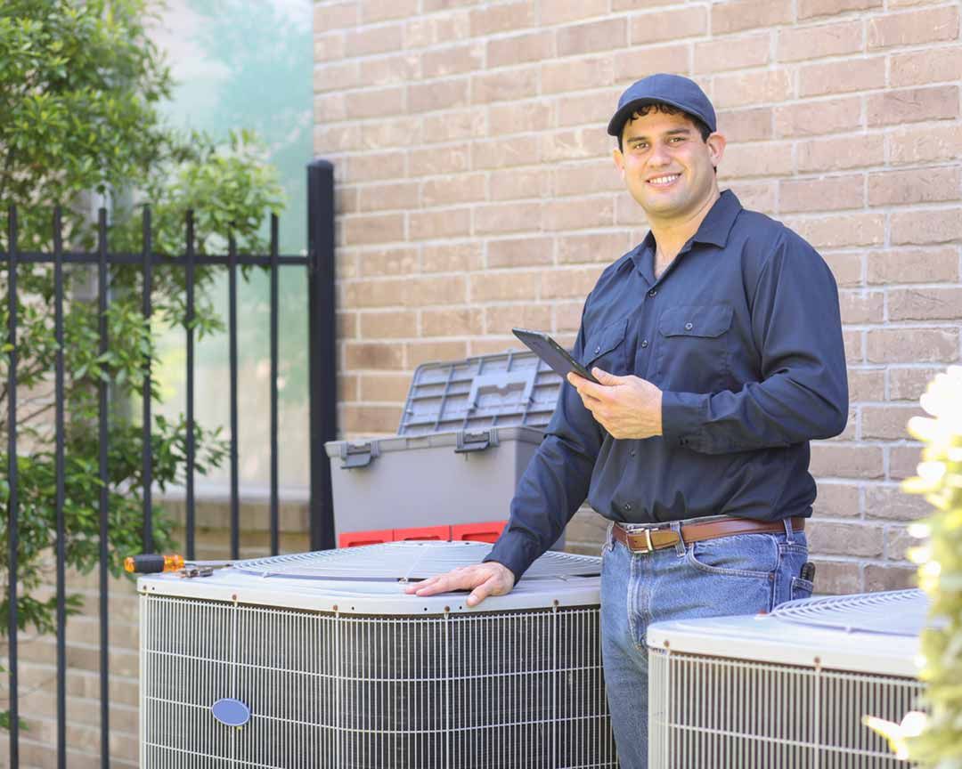 A man is standing next to two air conditioners and holding a tablet.