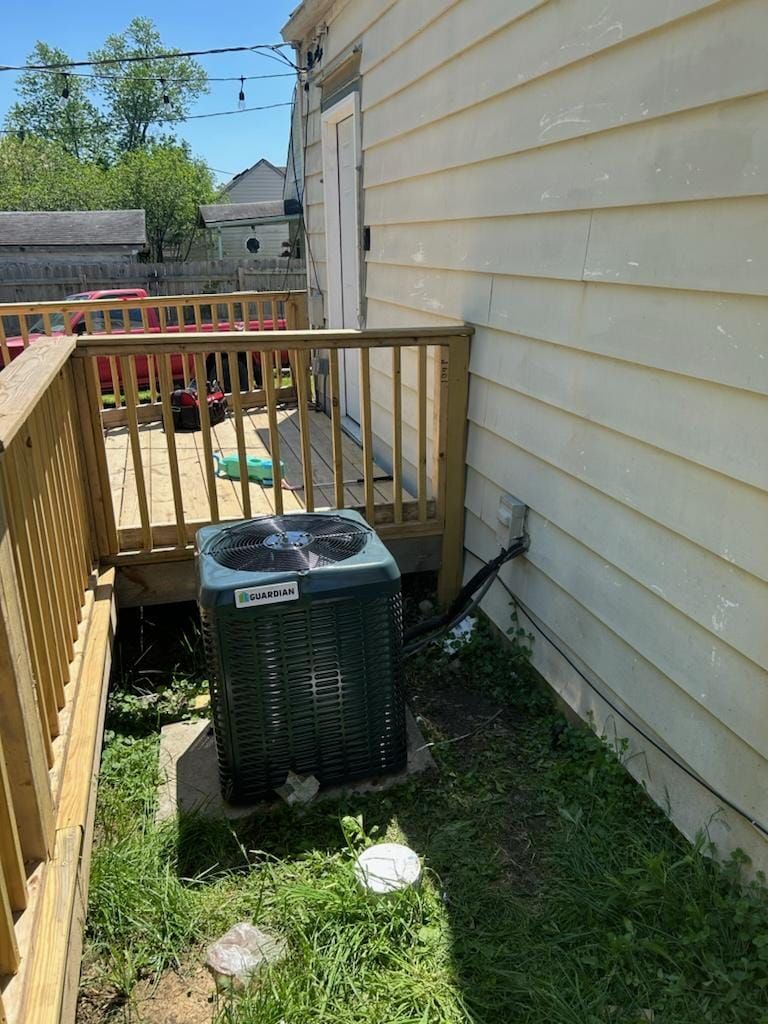 An air conditioner is sitting on the side of a house next to a deck.