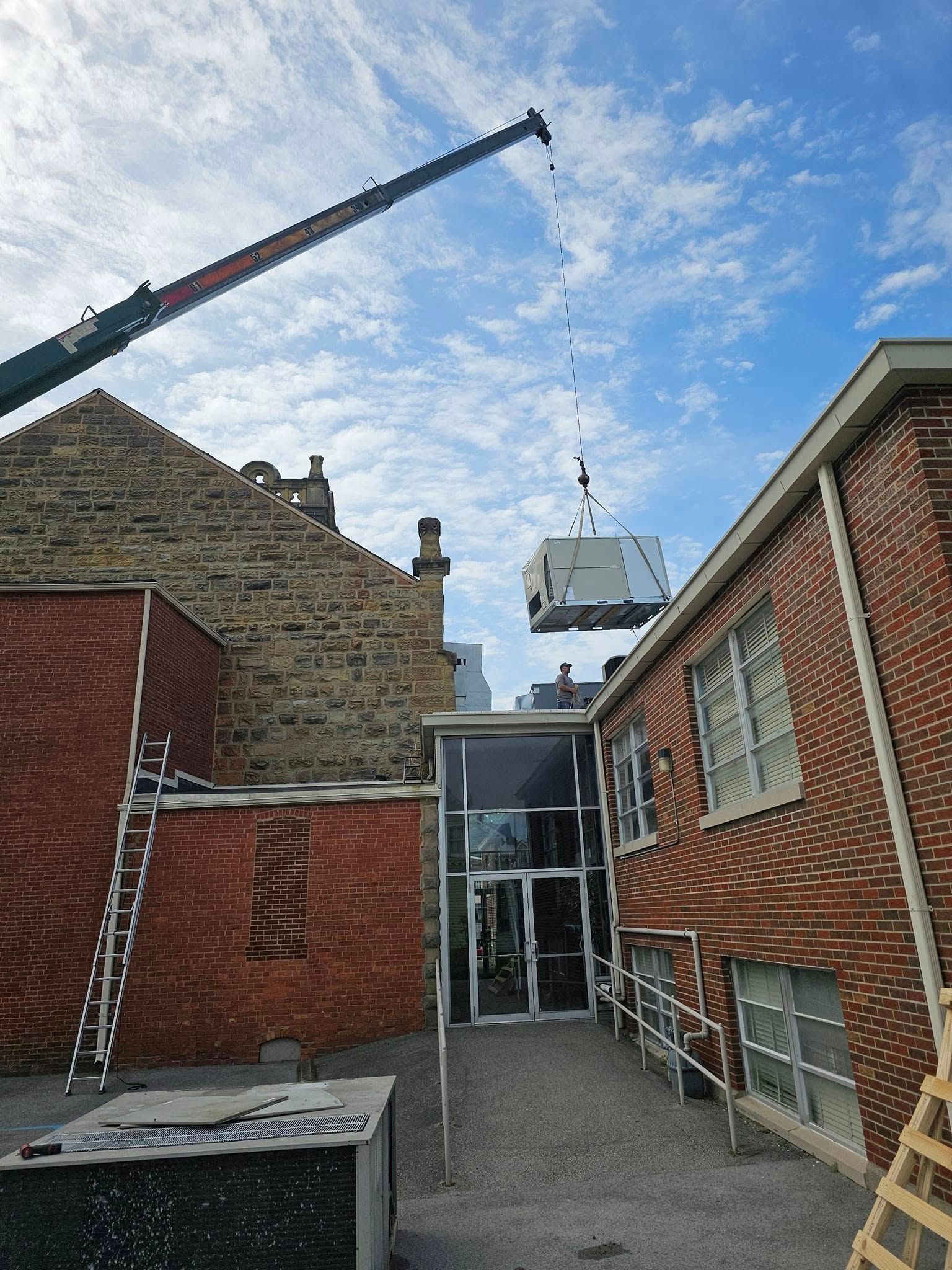 A crane is lifting a large piece of equipment on top of a brick building.