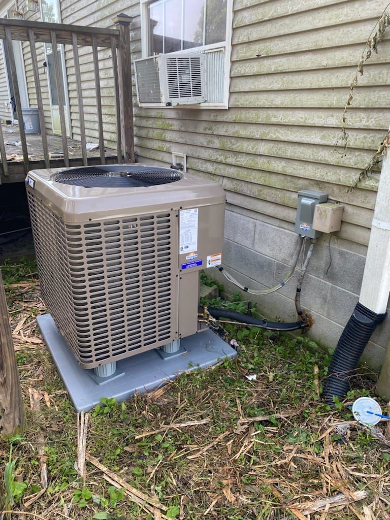 An air conditioner is sitting outside of a house next to a window.