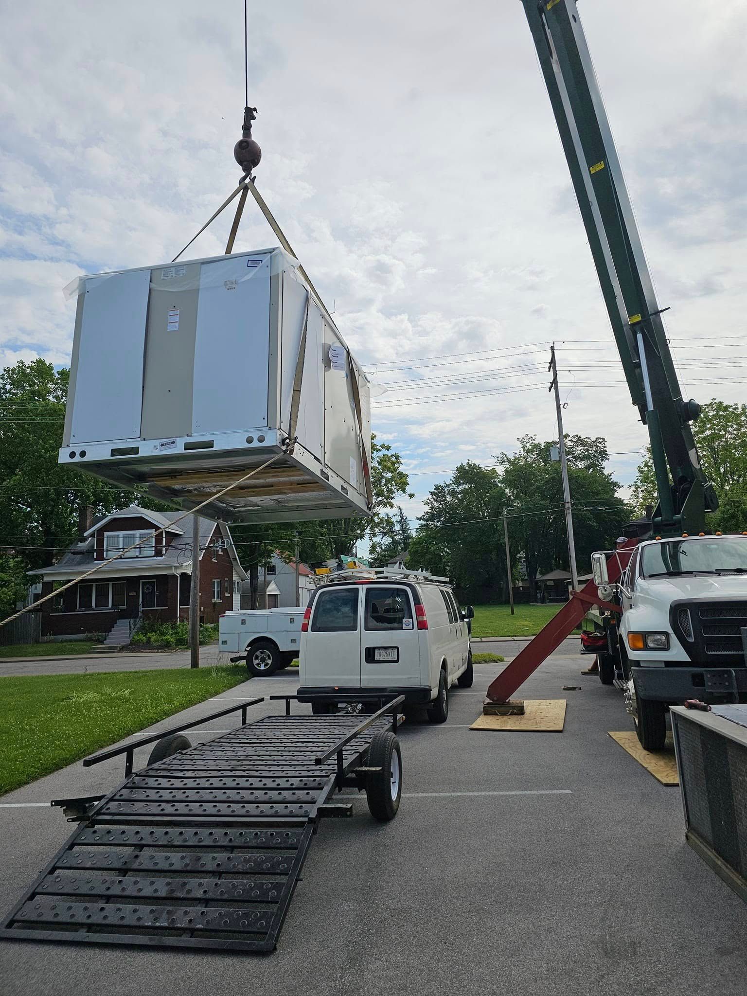 A white van is being lifted by a crane in a parking lot.